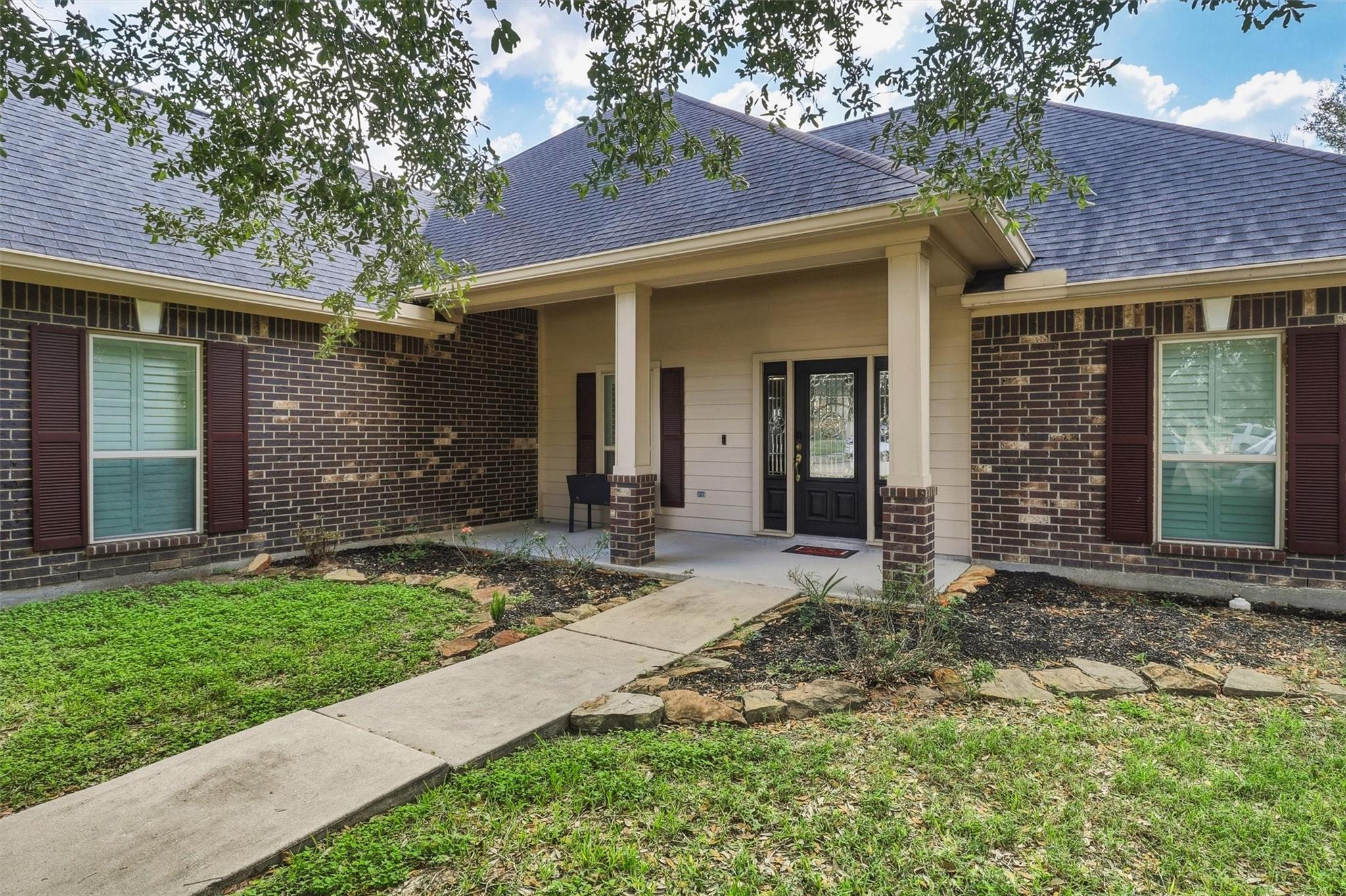 Brick house front with covered porch, dark entry door, and walkway through landscaped beds.