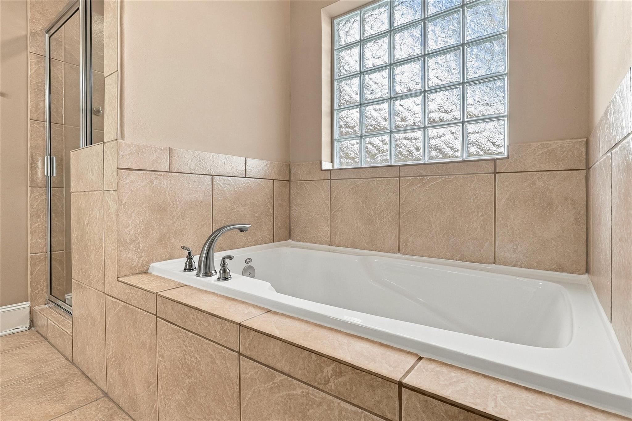 Bathroom with a tiled soaking tub, glass-block window, and adjacent glass-enclosed shower.