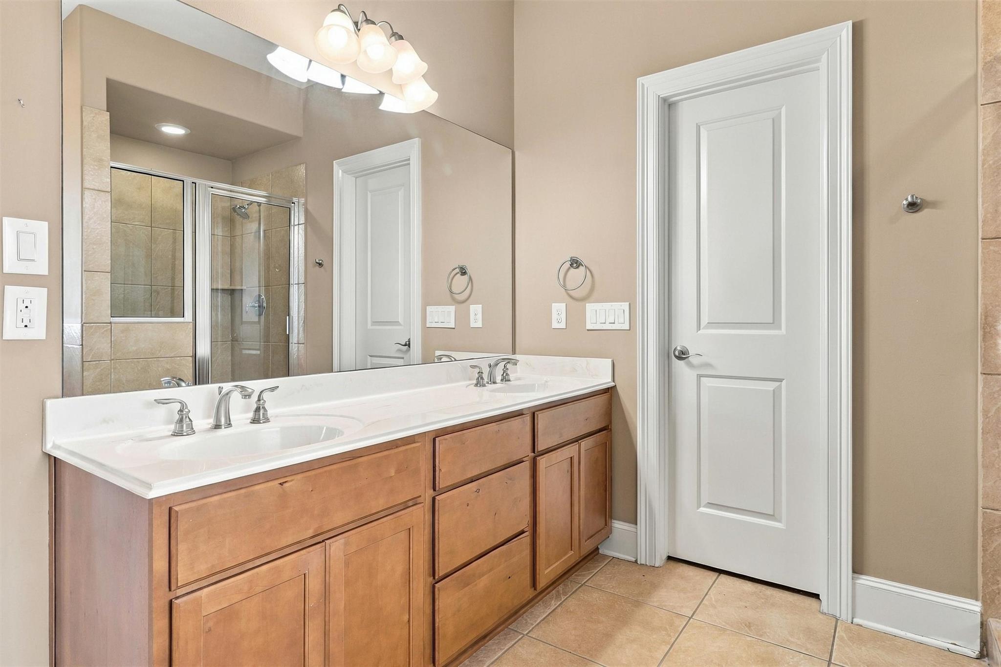Bathroom with a double-sink wood vanity and tiled glass-enclosed shower.
