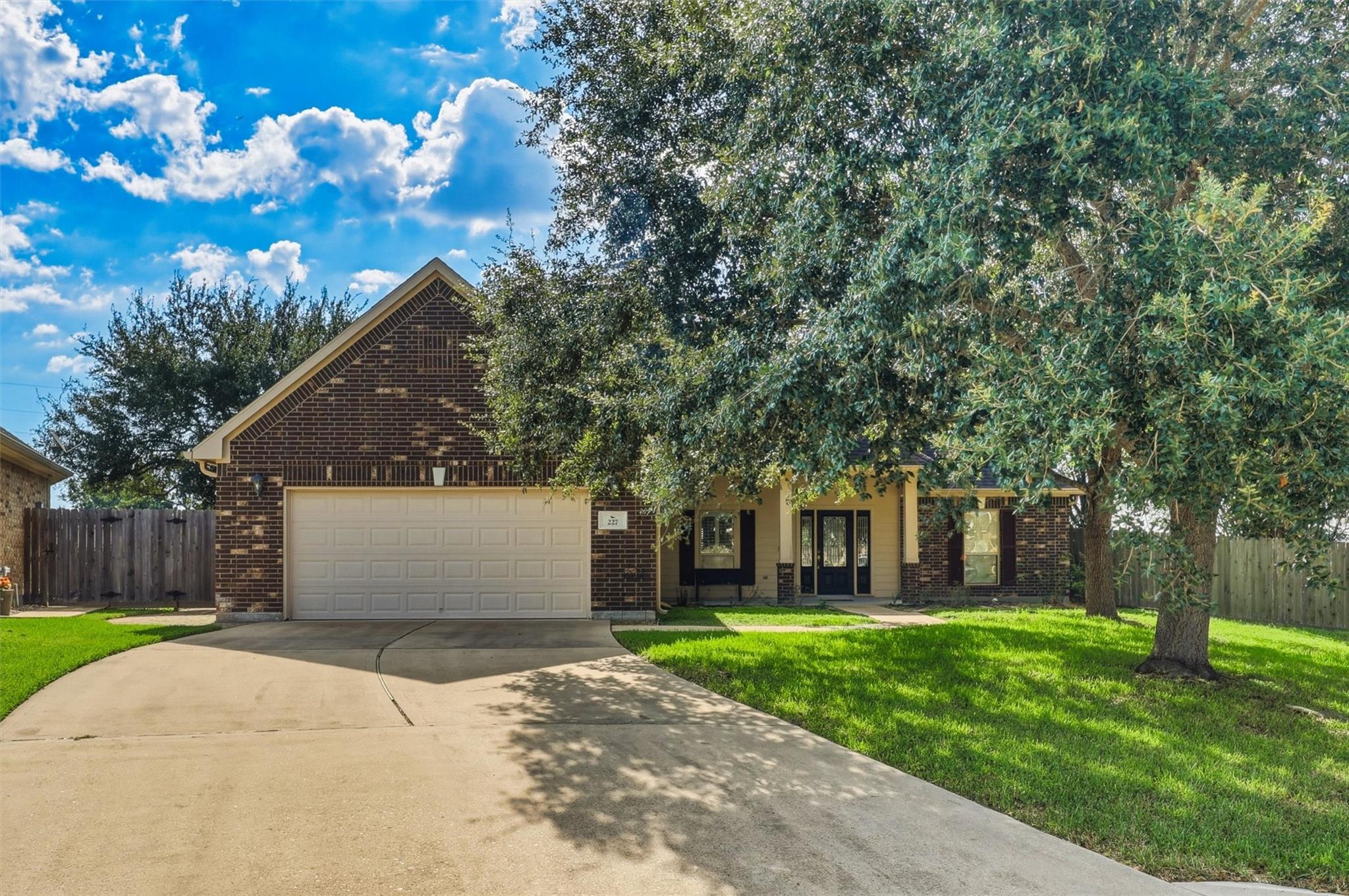 Brick two-story house with a two-car garage, broad driveway, and mature trees shading the front lawn.