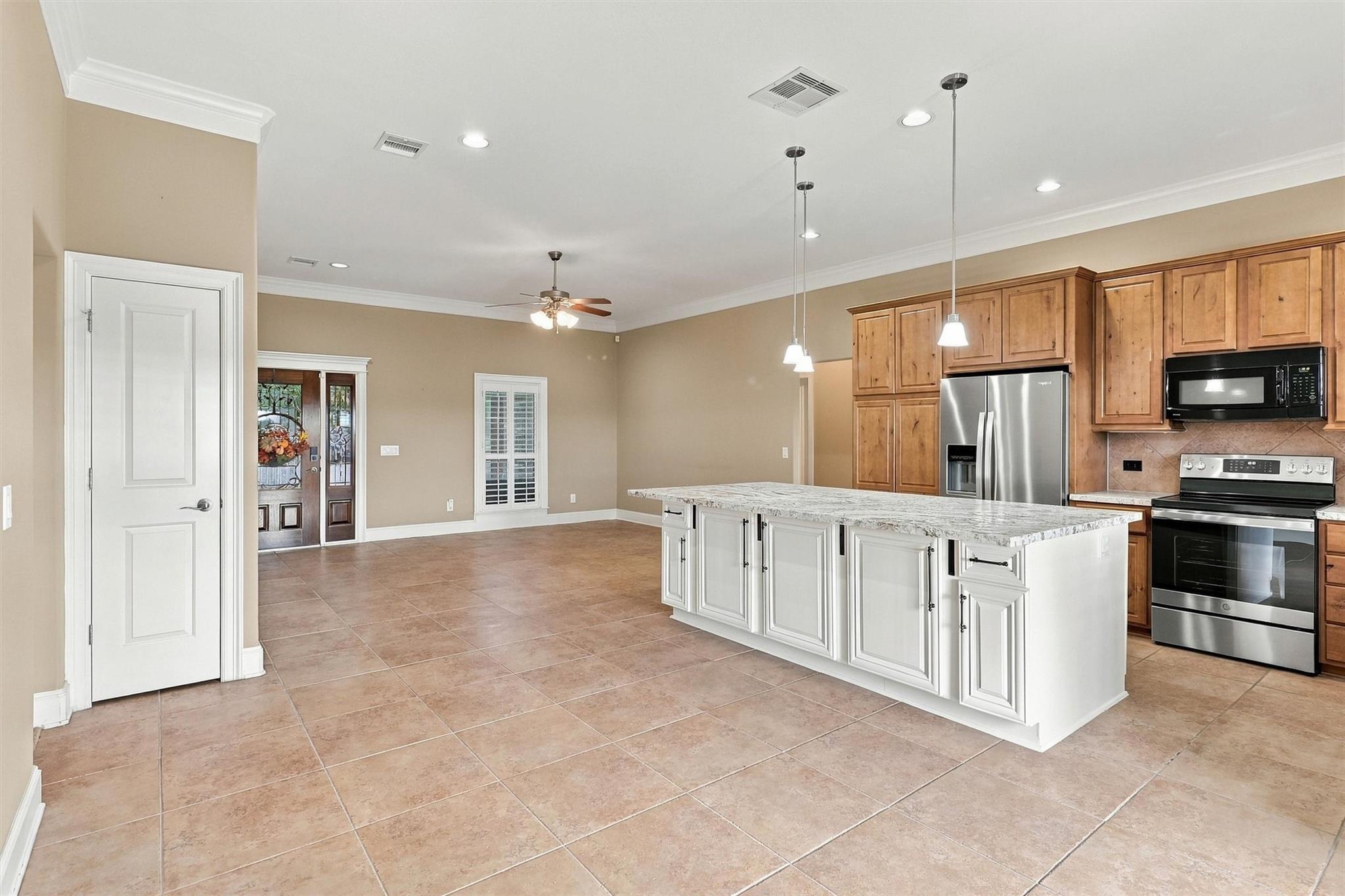 Kitchen with a large white island, wood cabinets, stainless steel appliances, and tan tile flooring.