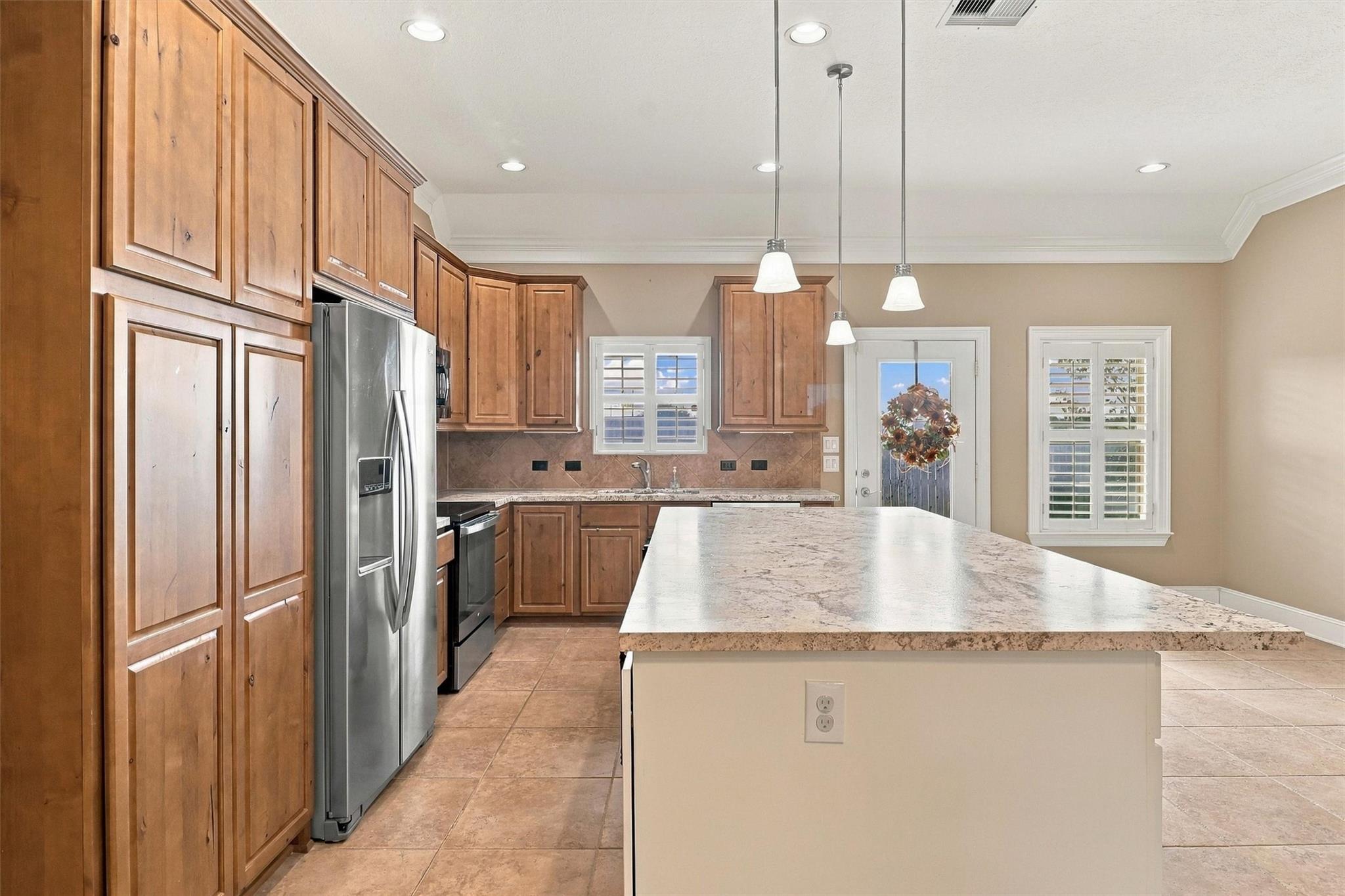 Kitchen with warm wood cabinets, a large stone island, stainless appliances, and plantation shutters.