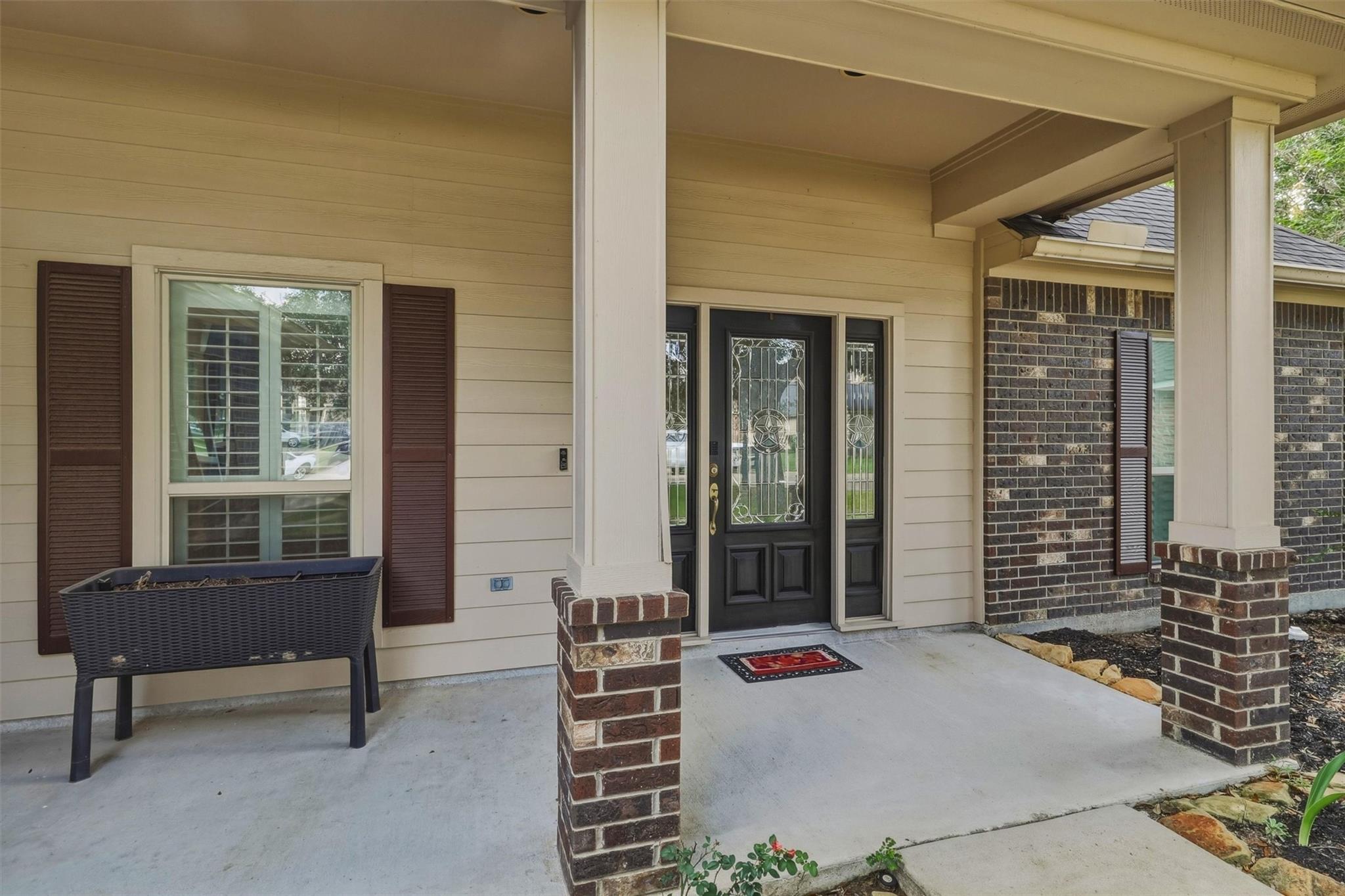 Covered front porch with brick columns, a black glass-paneled door, and a shuttered window.