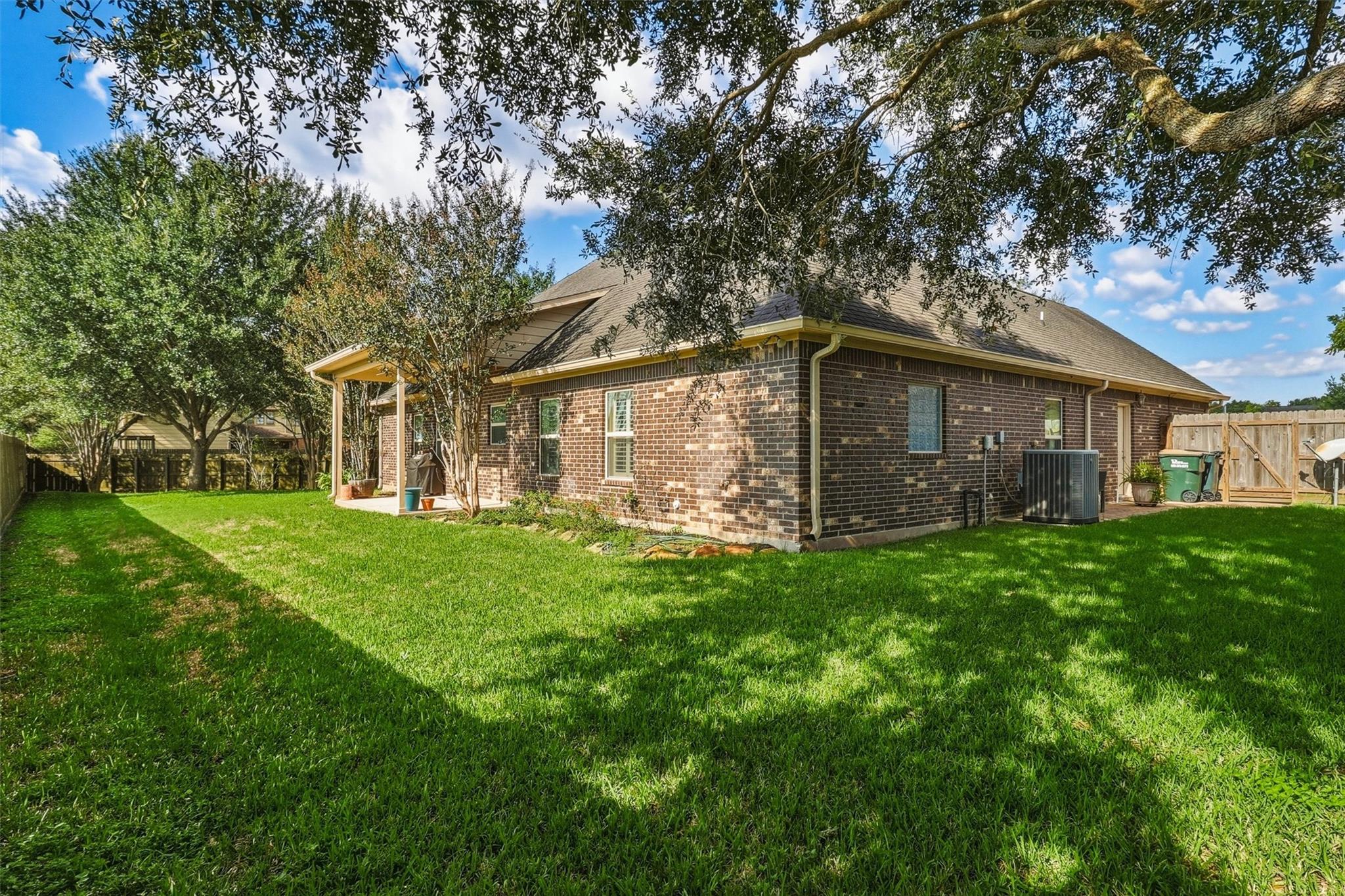 Single-story brick house and covered patio beyond a broad lawn shaded by mature trees.