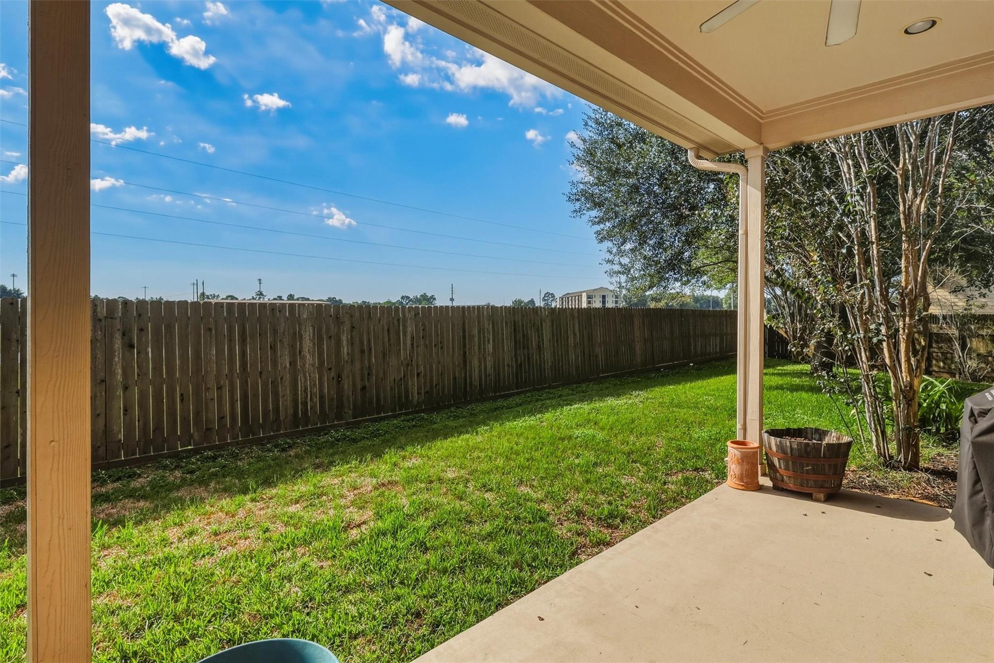 Covered patio overlooking a fenced grassy backyard with trees and planters.