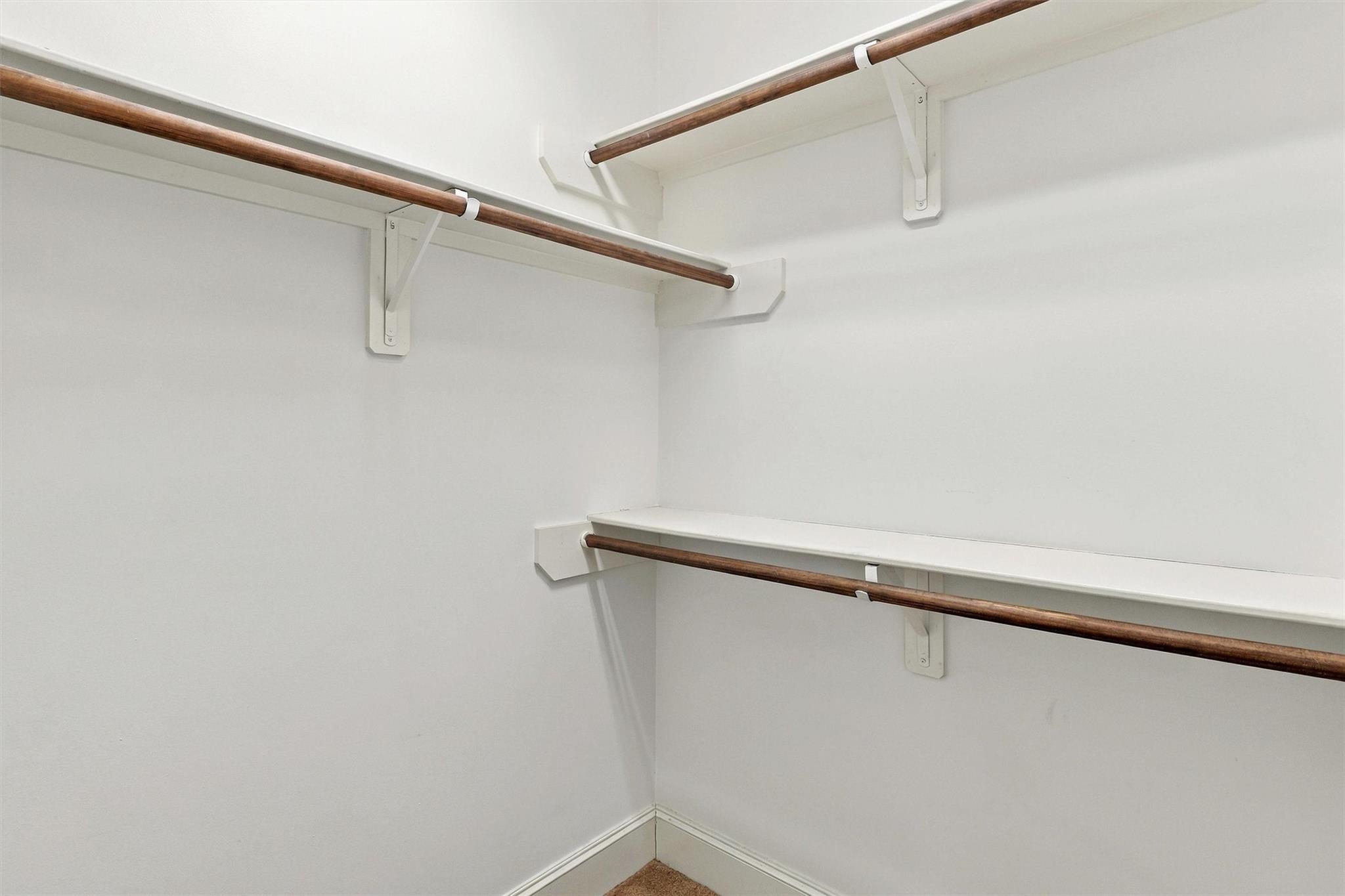 Empty white closet with three dark wood hanging rods and beige carpet.