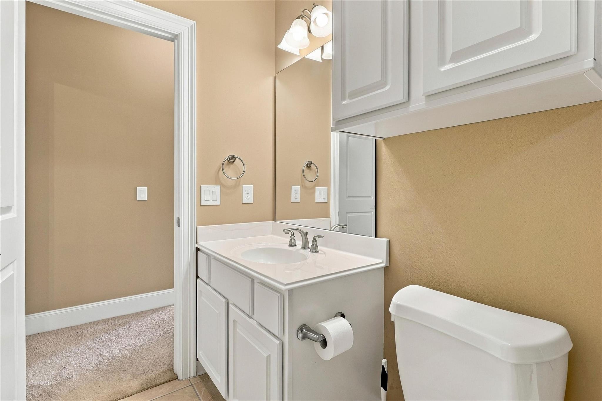 Bathroom with a white vanity, mirrored cabinet, and toilet beside an open doorway.