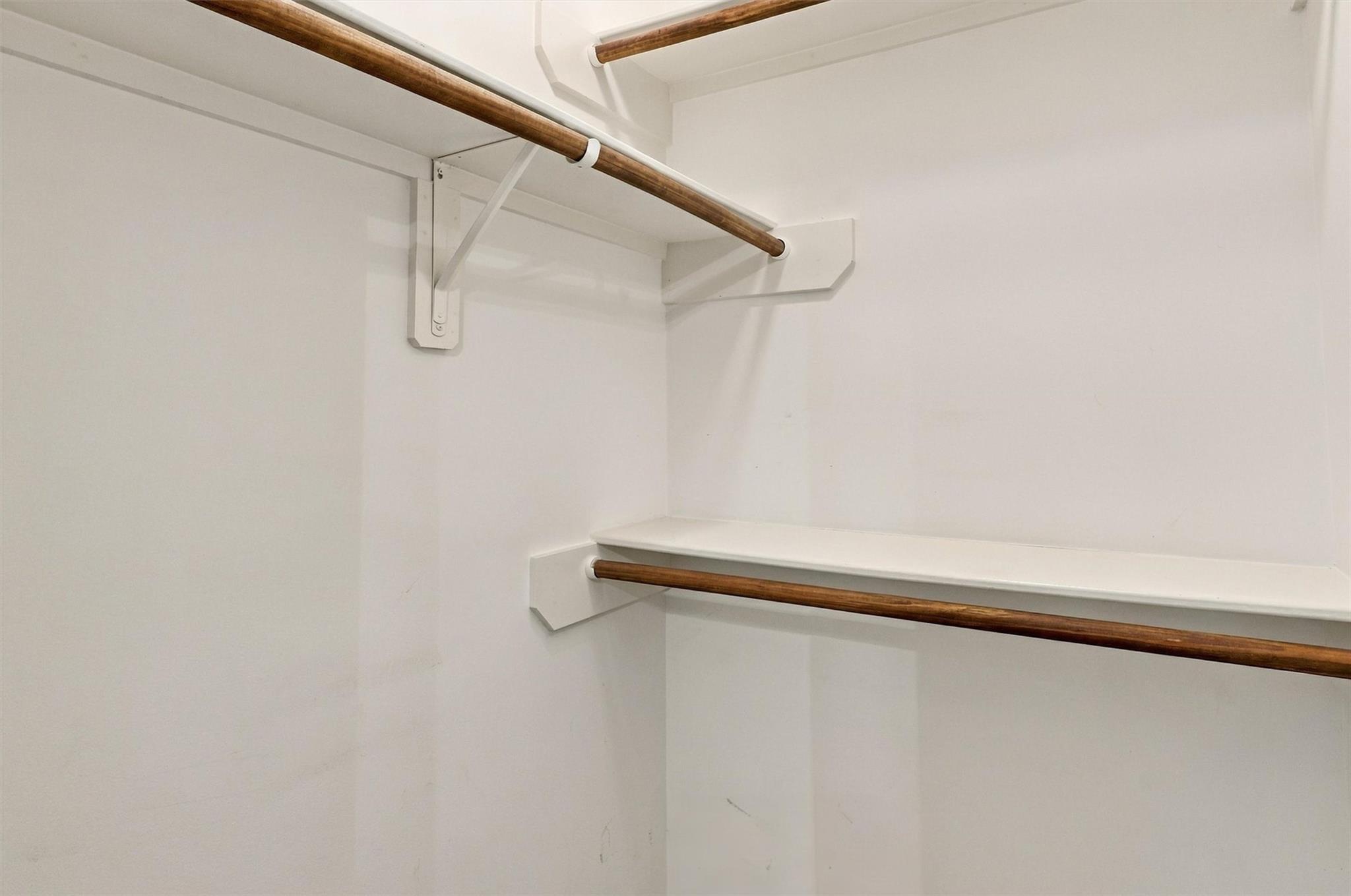 Empty white closet with built-in shelf and two wooden hanging rods.