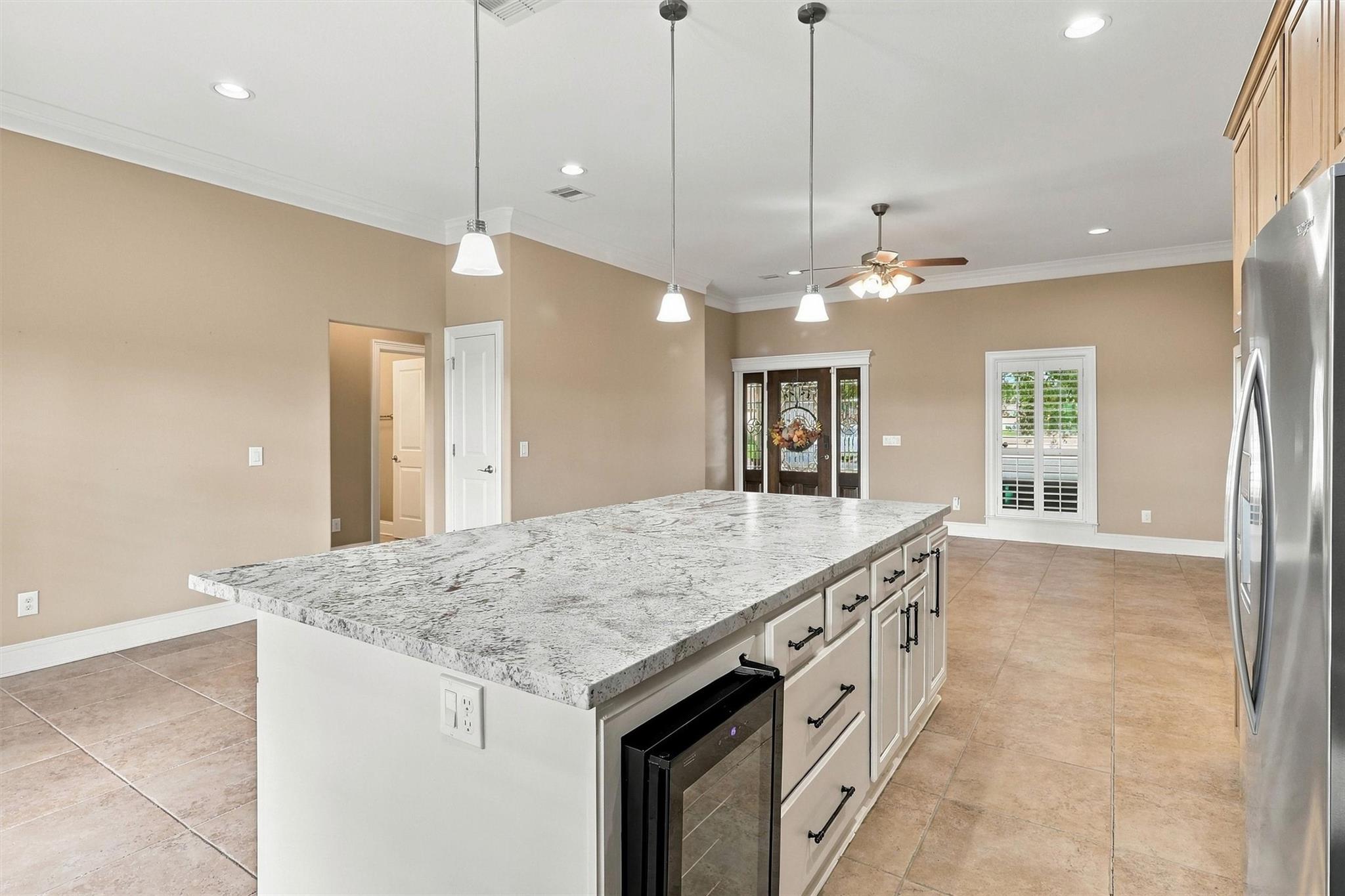 Kitchen with a large granite island, white cabinetry, and stainless steel appliances.