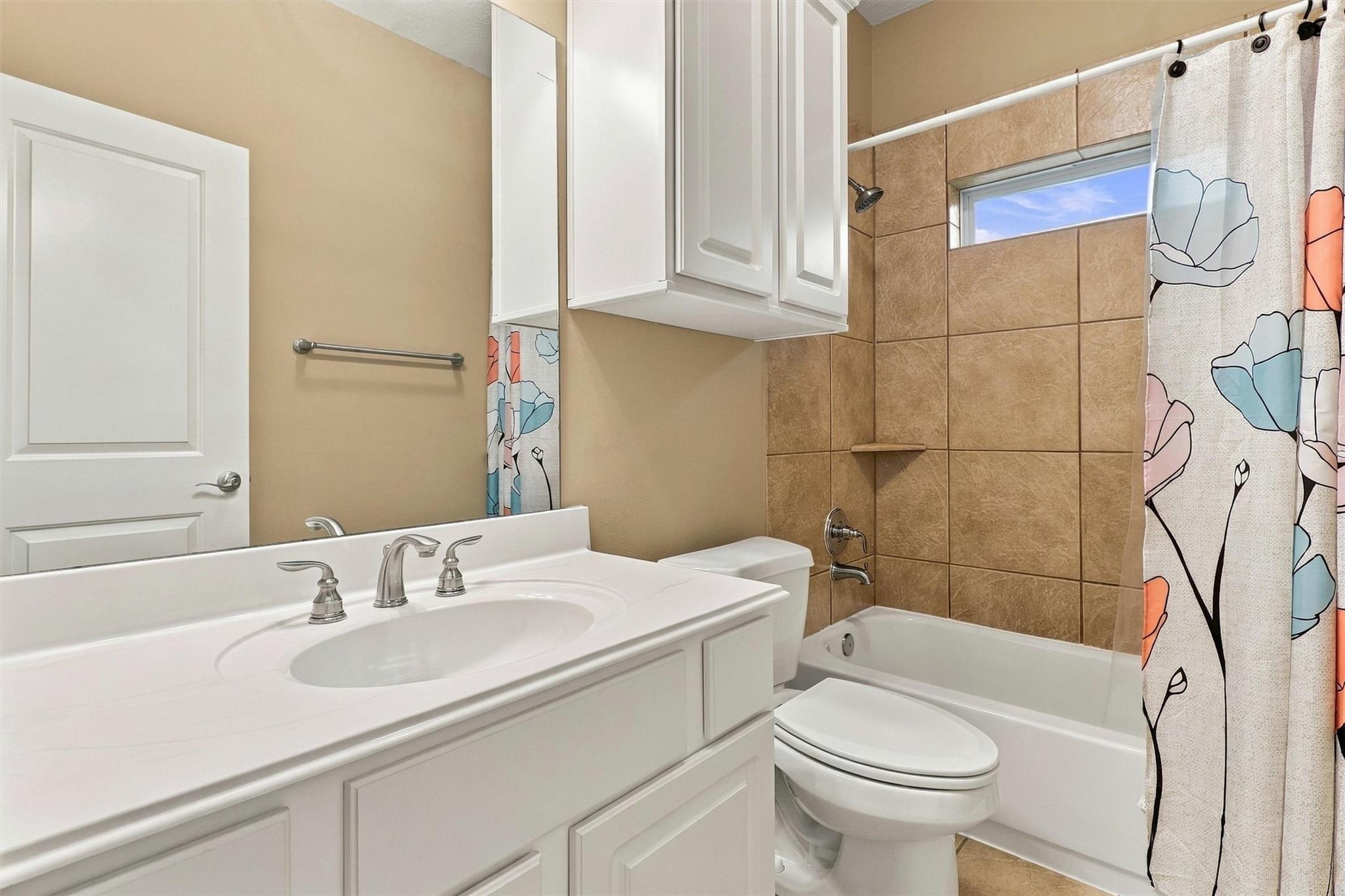 Bathroom with a white vanity, tan tiled tub surround, and floral shower curtain.