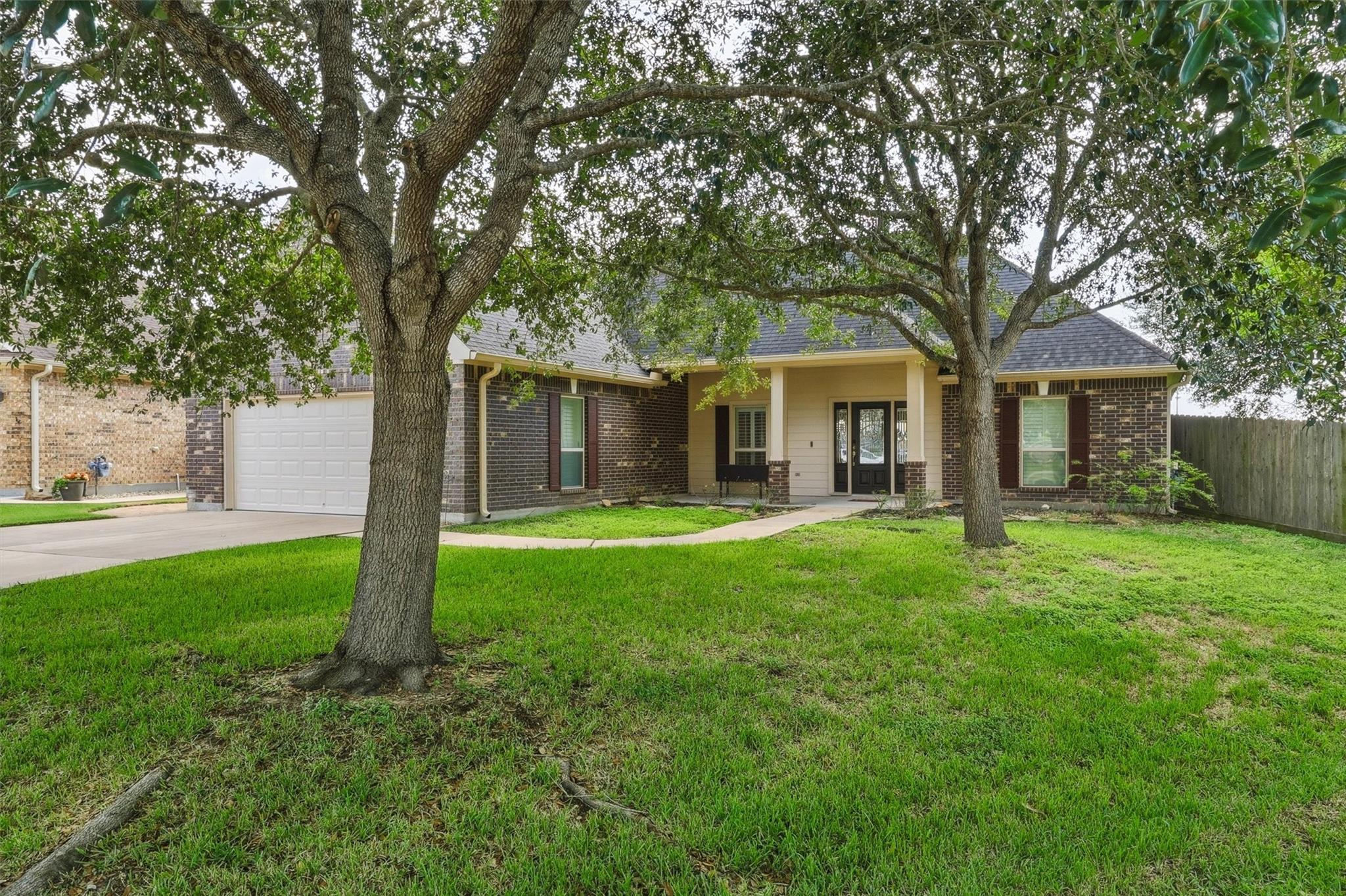 Single-story brick home with an attached garage, covered entry, and two large shade trees across the lawn.