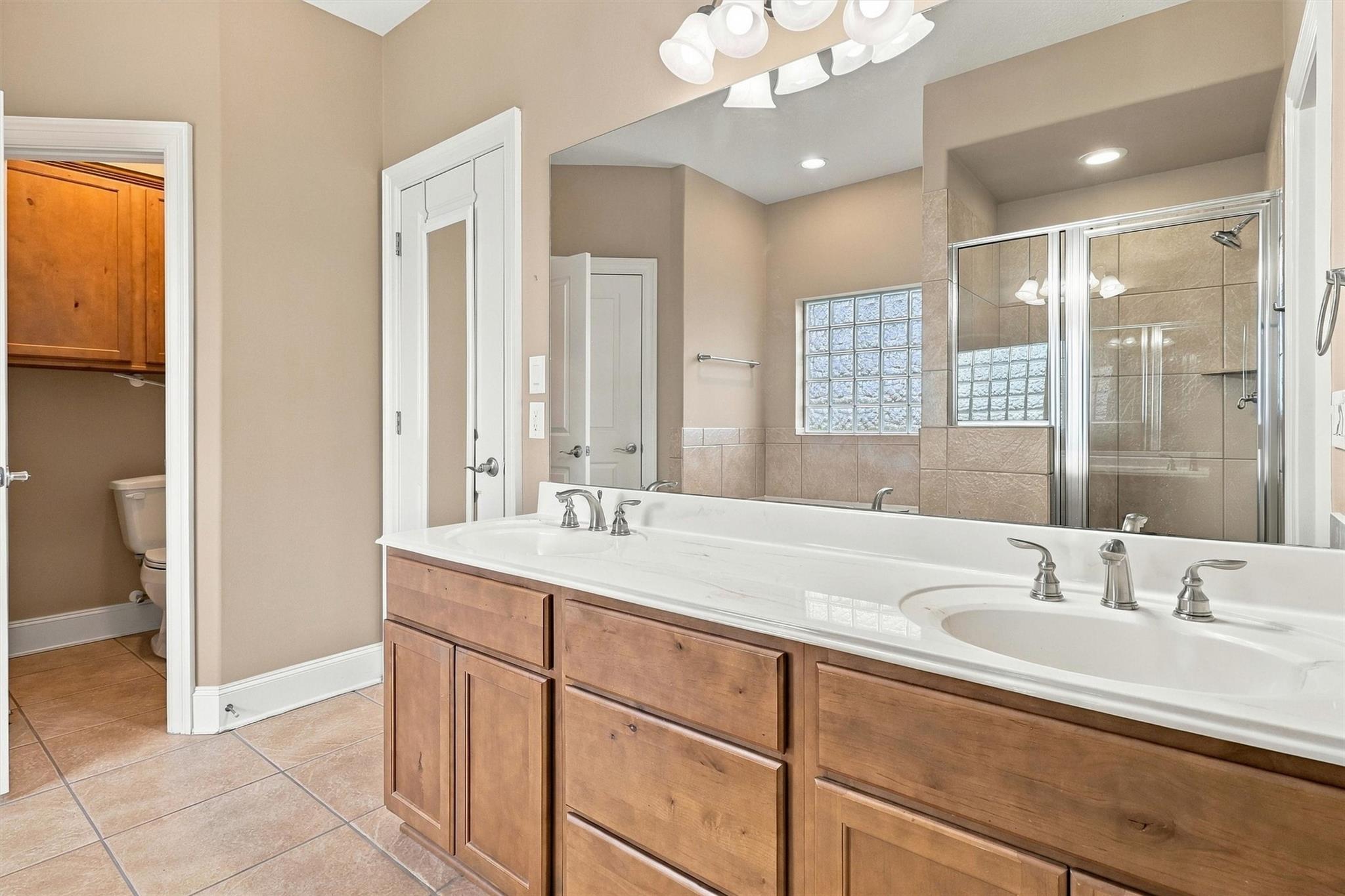 Primary bathroom with double-sink wooden vanity, mirrored wall, and tiled glass shower.