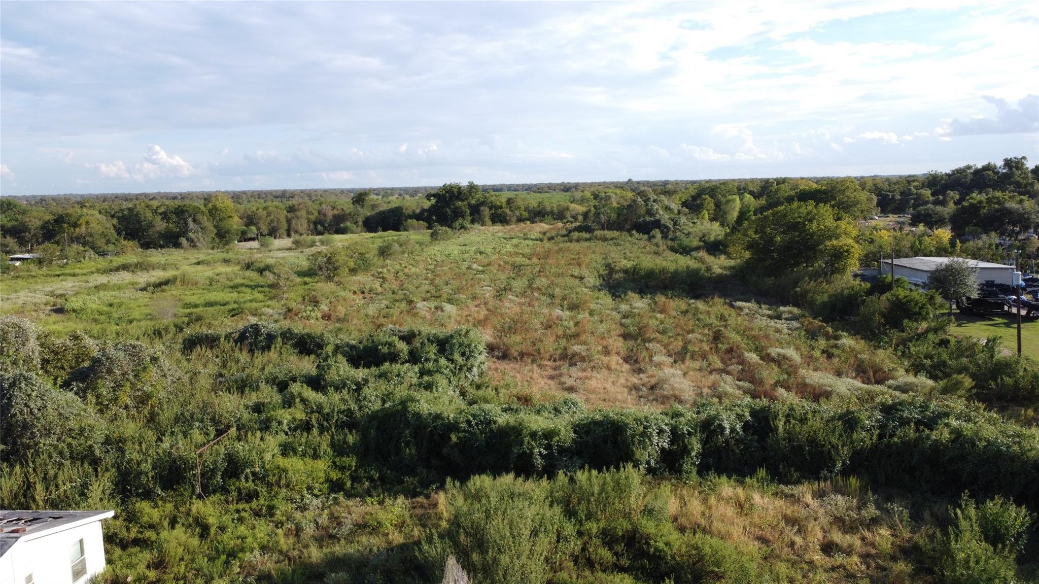 Aerial view of brush-covered land bordered by trees, with a metal-sided building at the right edge.