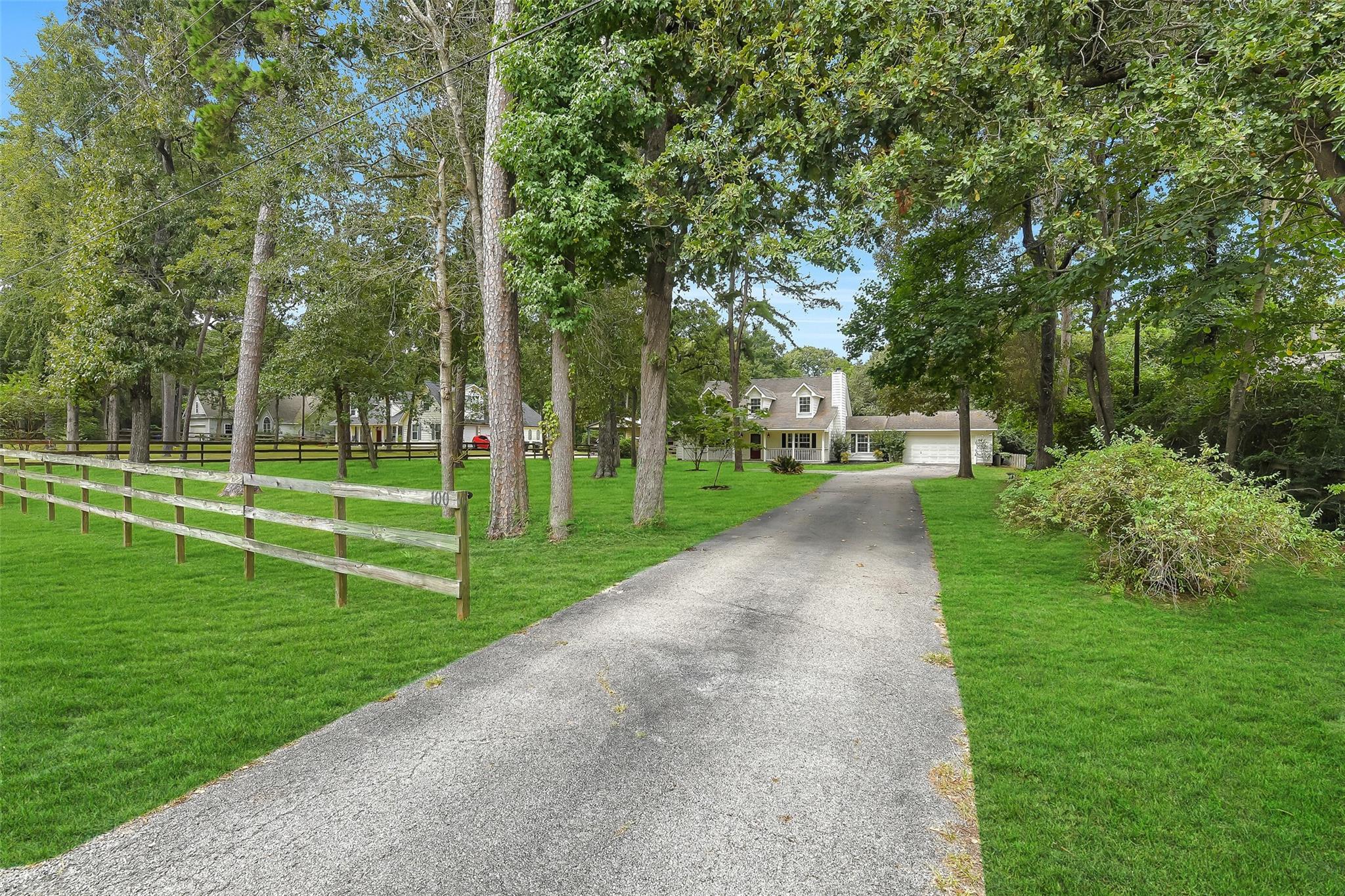 Two-story house with attached garage at the end of a tree-lined driveway and fenced lawn.
