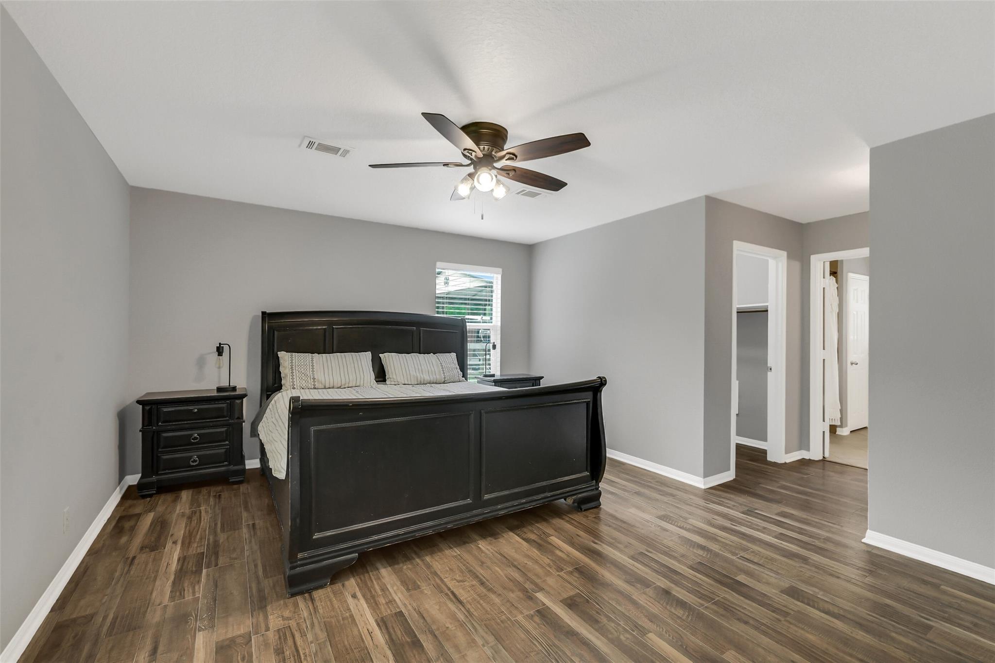 Bedroom with a dark wood bed, plank flooring, and a ceiling fan.