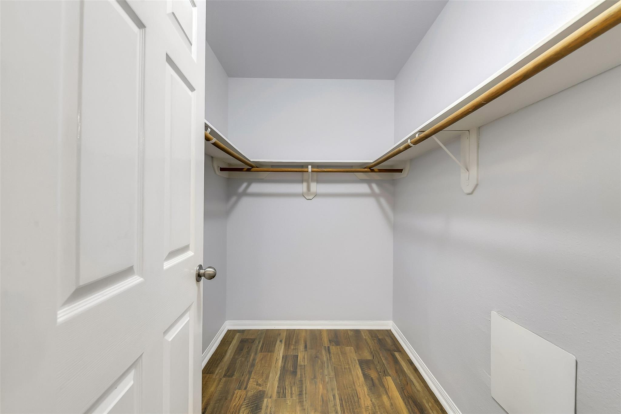 Empty walk-in closet with wood-look flooring and wooden clothes rods along three walls.