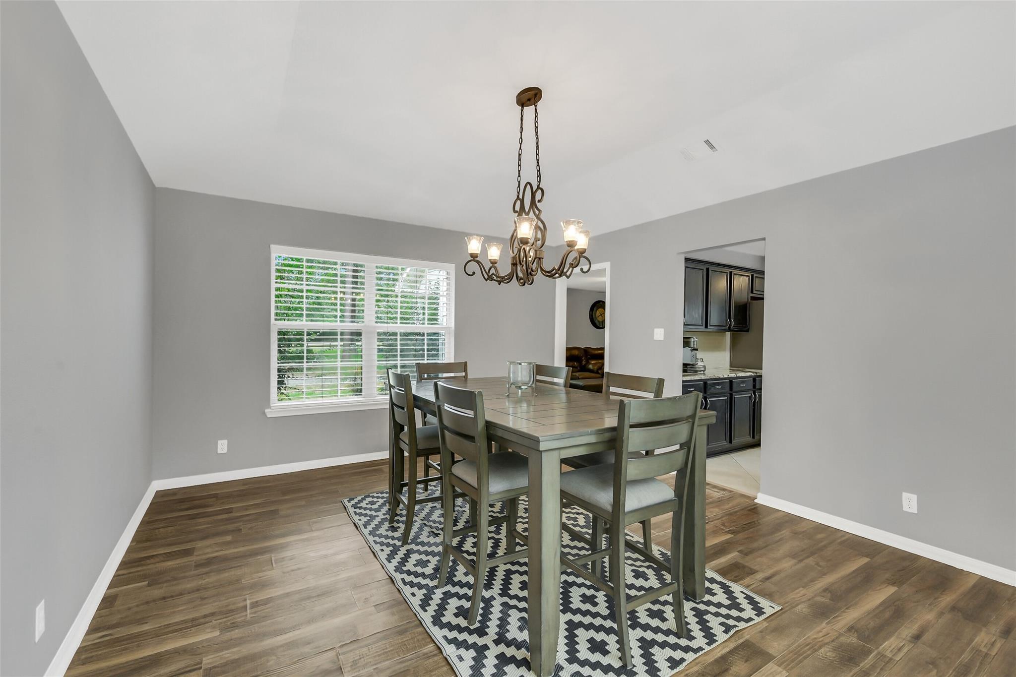 Dining room with a rectangular table, patterned rug, chandelier, and large window.