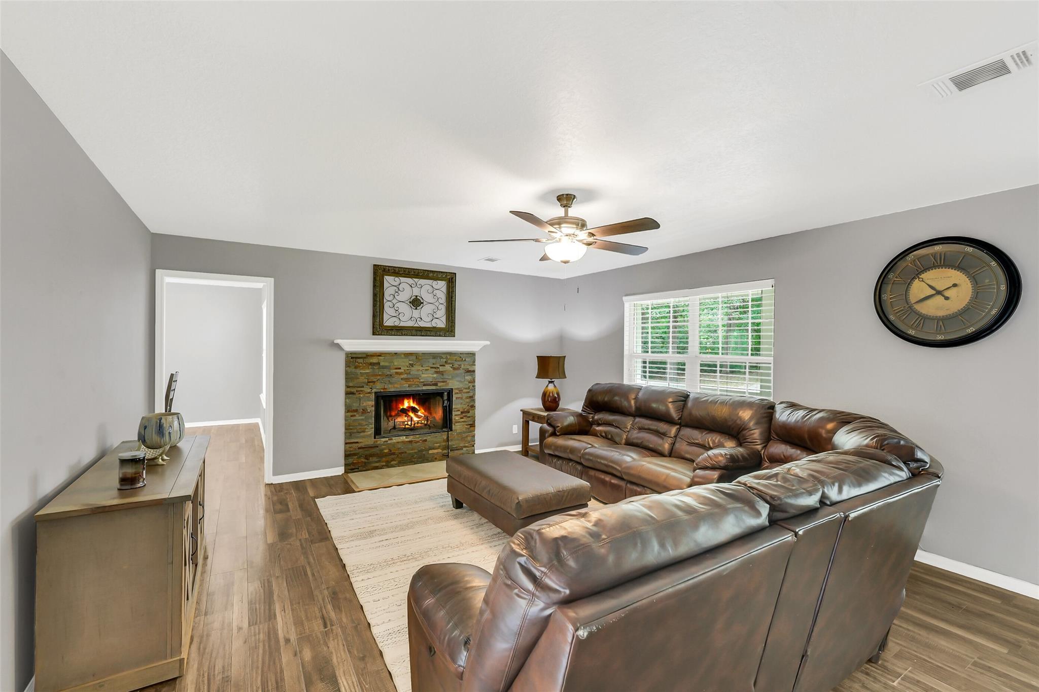 Living room with a brown leather sectional and a stone fireplace with a lit fire.