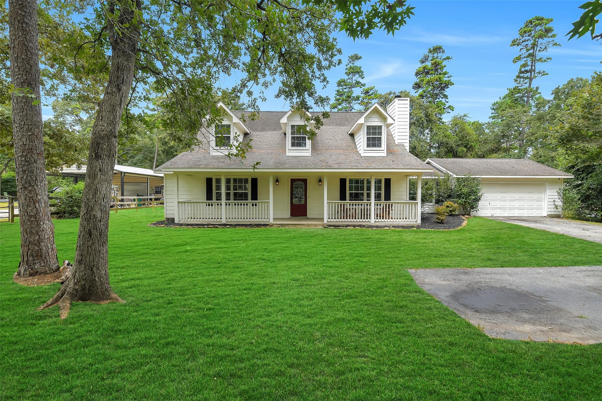 White two-story house with a covered porch, attached garage, and mature trees across a broad lawn.