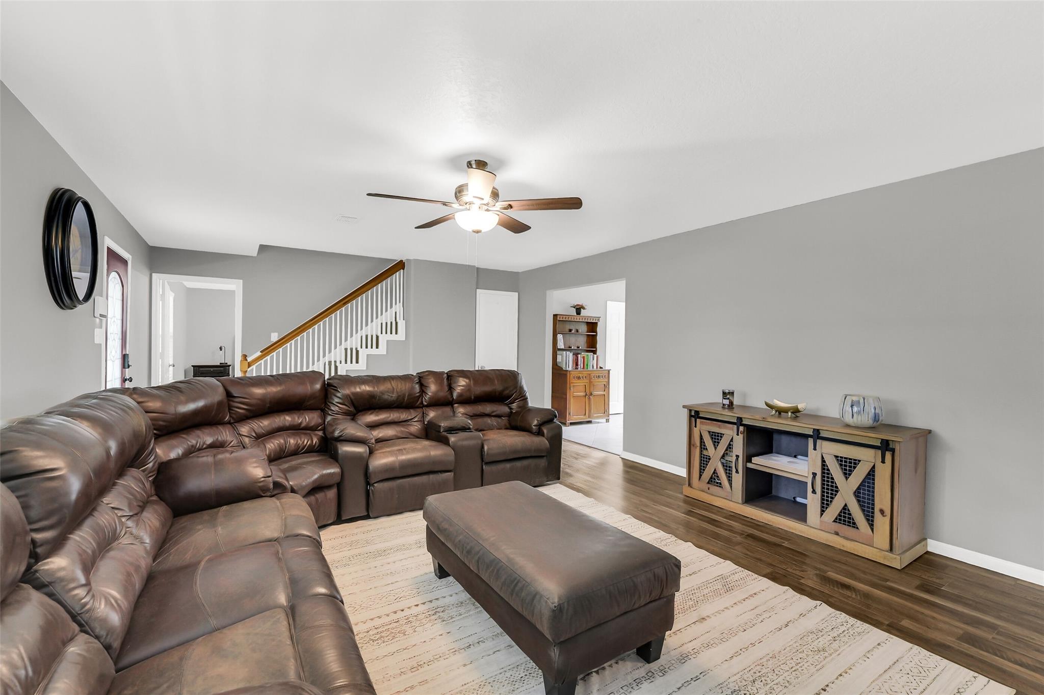 Living room with a brown leather sectional, matching ottoman, and staircase with white balusters.
