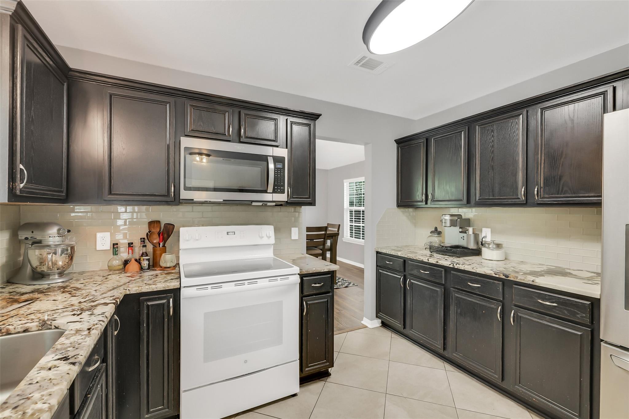 Kitchen with dark wood cabinets, stone counters, and a white range and microwave.
