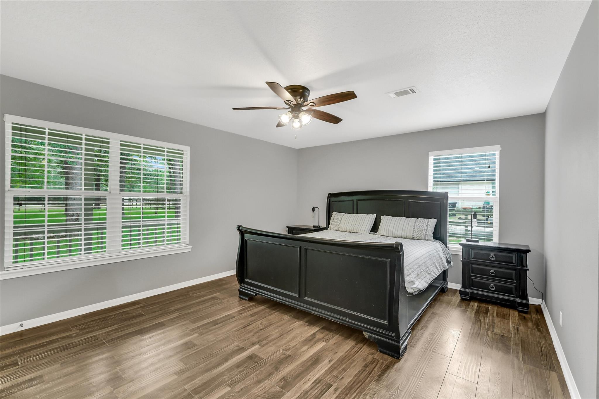 Bedroom with a dark wood bed, wood-look flooring, shuttered windows, and ceiling fan.