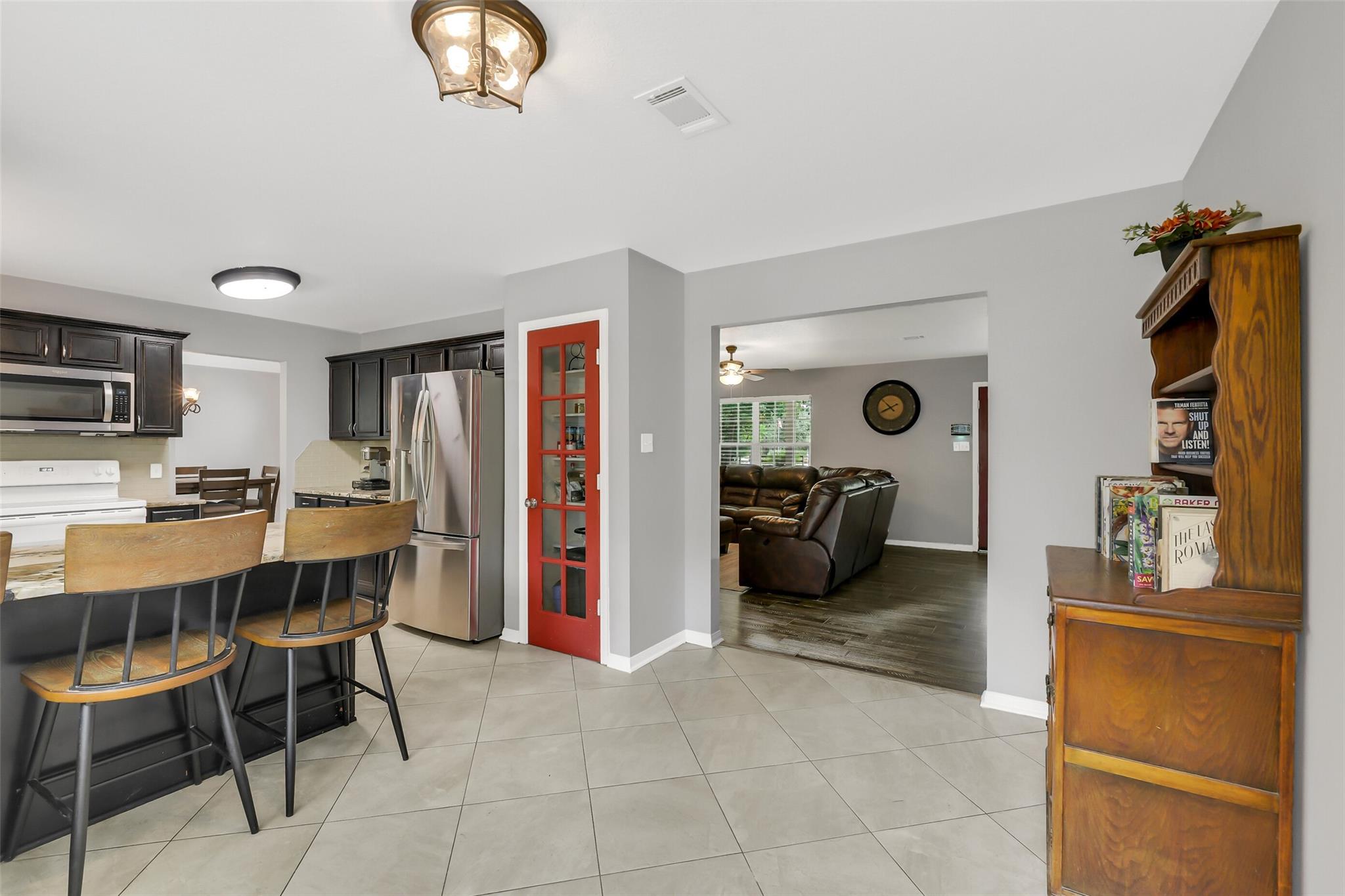 Kitchen and dining area with dark cabinets, a breakfast bar, stainless appliances, and a red glass-paneled door.