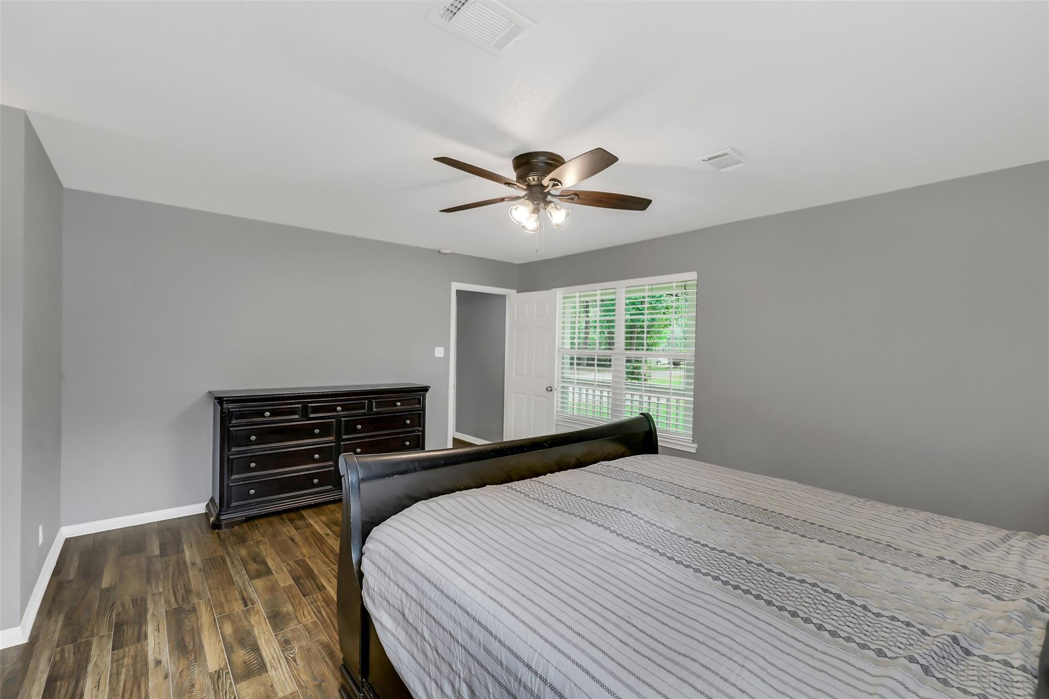 Bedroom with a dark bed and dresser, wood-look flooring, and a window with white shutters.