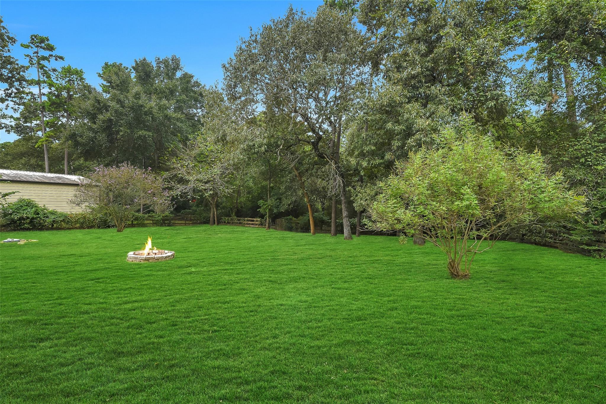 Spacious backyard with a circular stone fire pit, broad lawn, and mature trees.