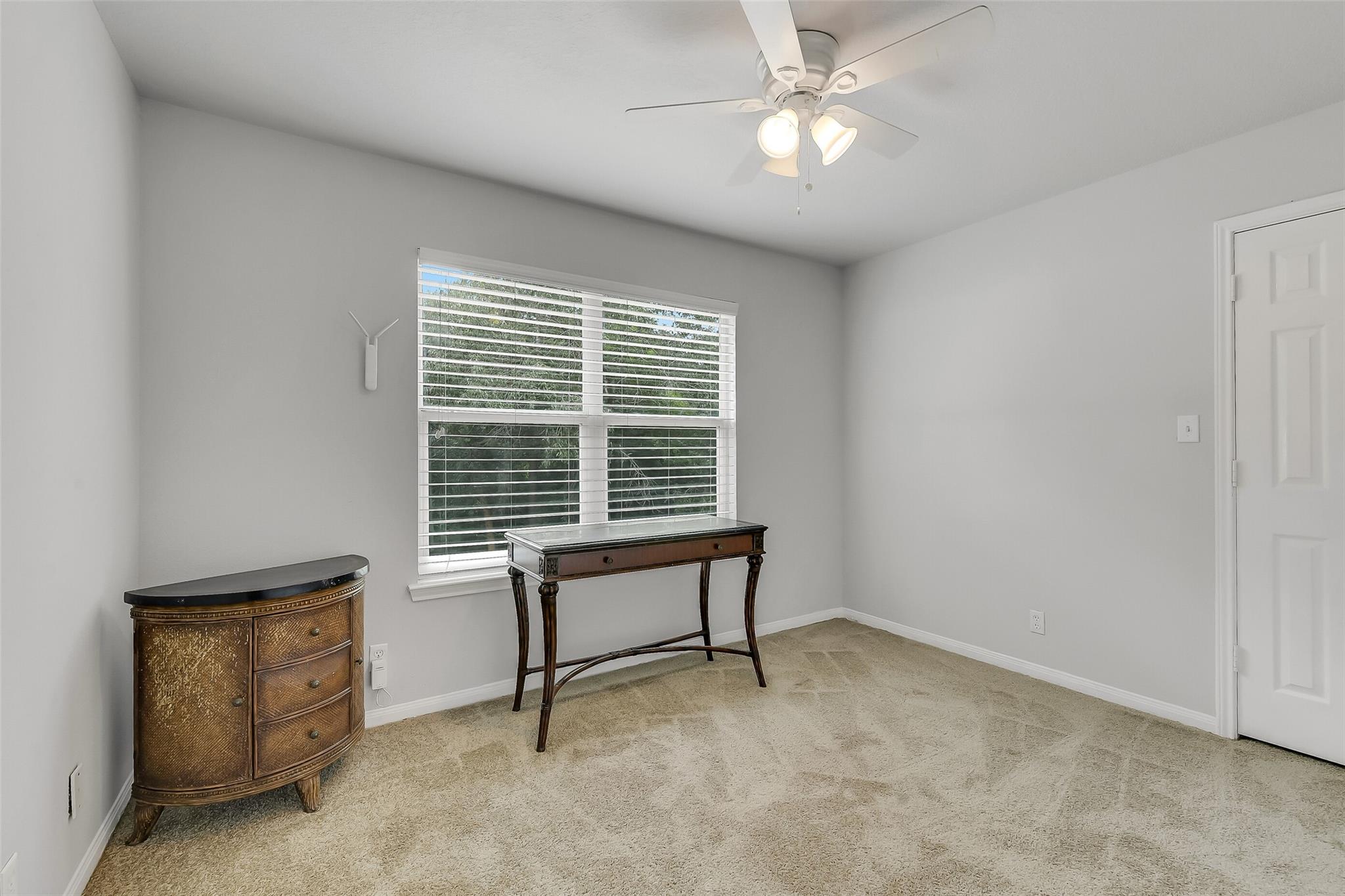 Carpeted room with a large window, ceiling fan, and two dark wood furniture pieces.