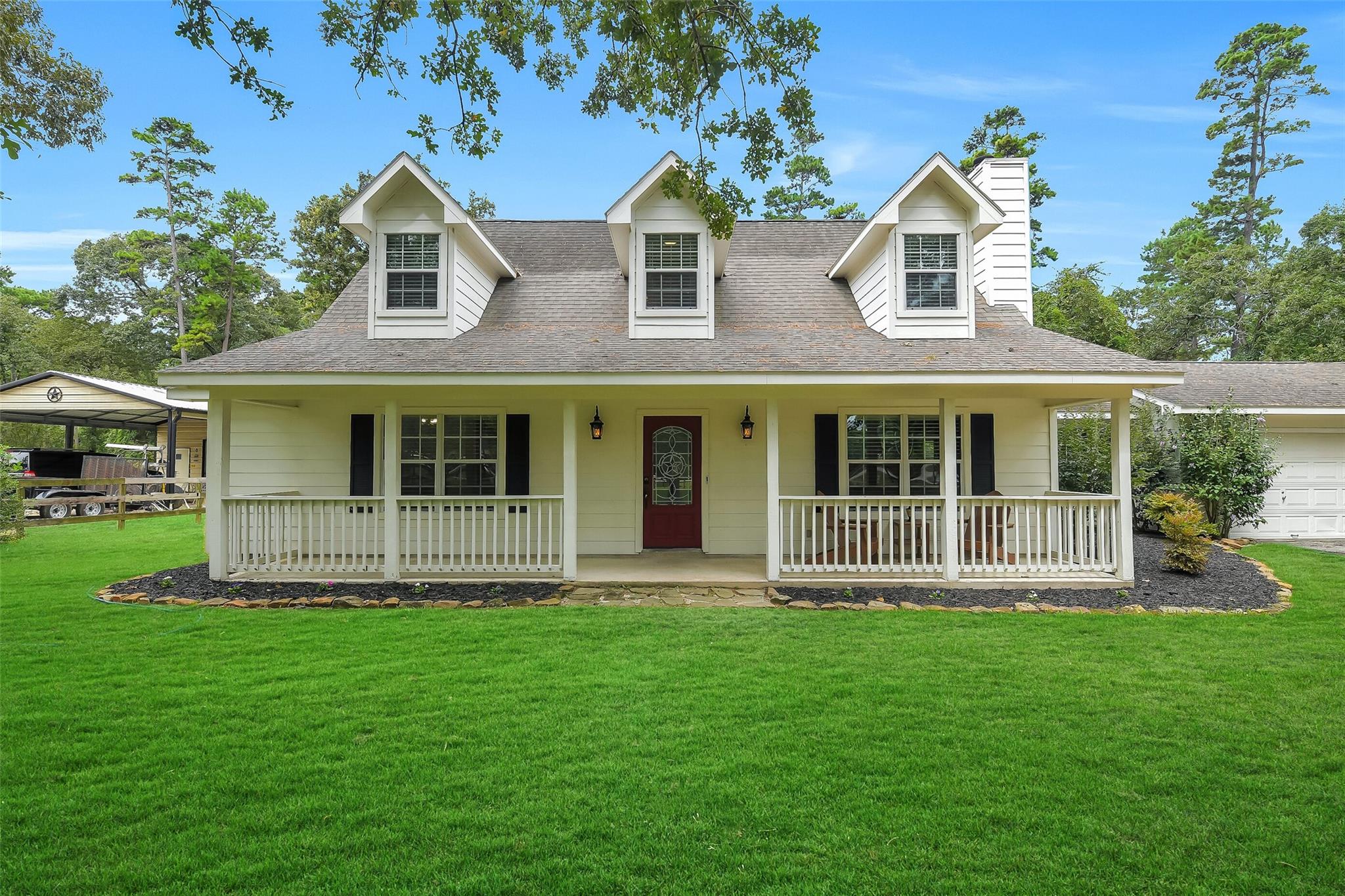 White two-story home with three dormers, a broad covered porch, and a red front door.