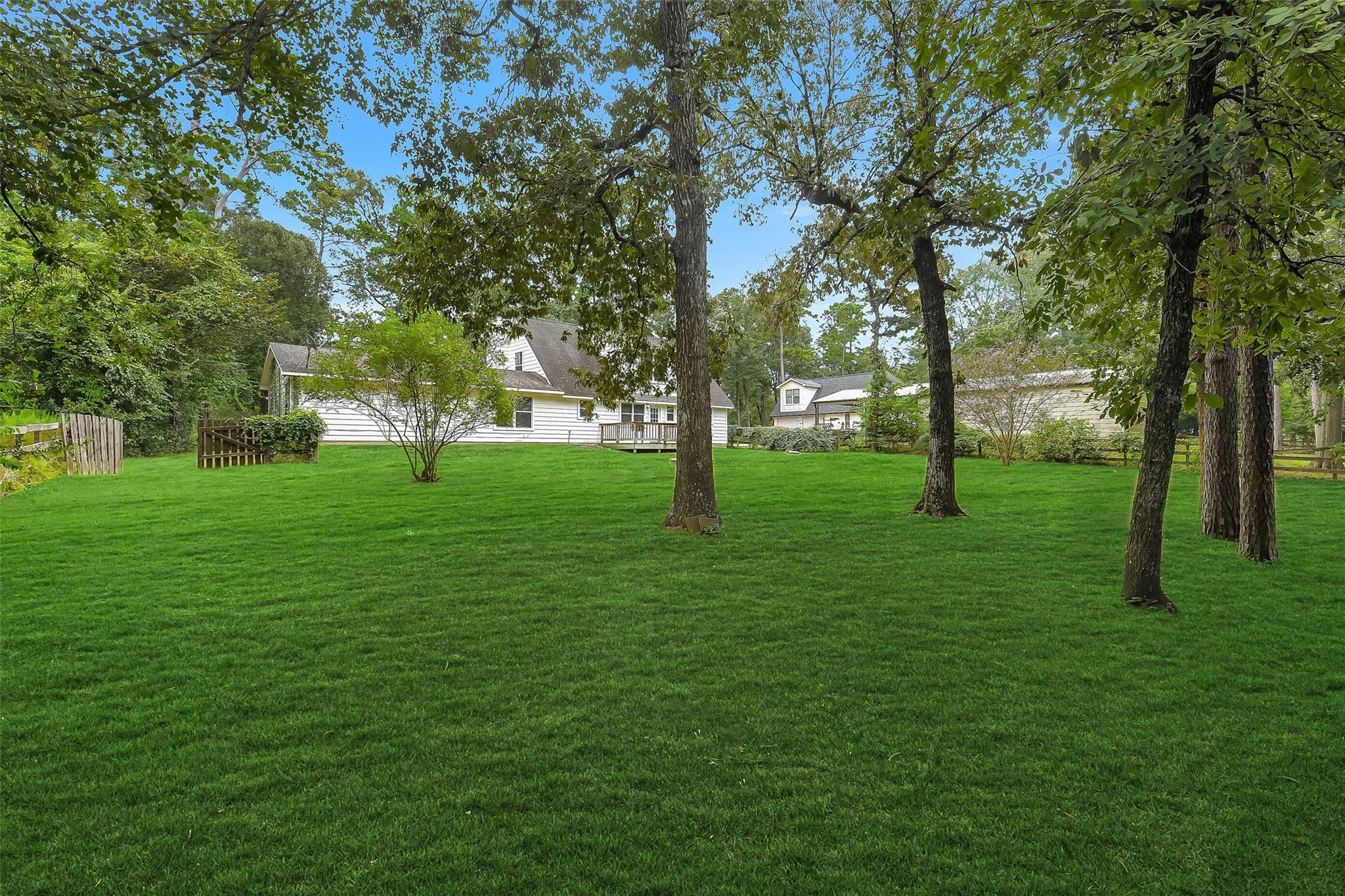 White house beyond a broad lawn, framed by mature trees and a wooden fence.