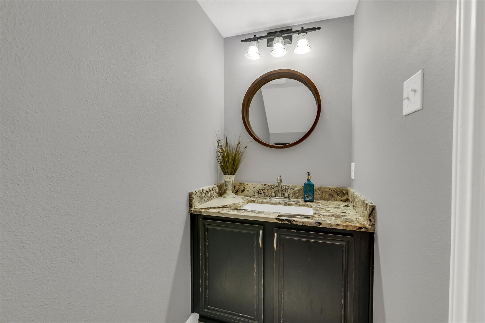 Bathroom vanity with a mottled stone counter, dark cabinet, and round wood-framed mirror.