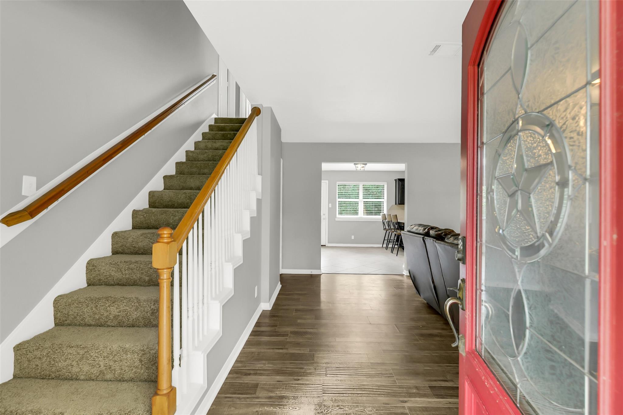 Entryway with a carpeted staircase, dark wood-look flooring, and an open red front door.