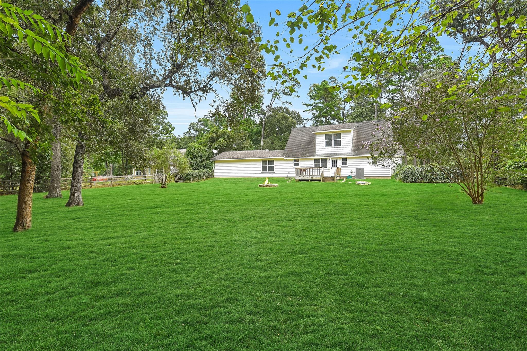 White-sided house and small deck beyond a broad lawn shaded by mature trees.