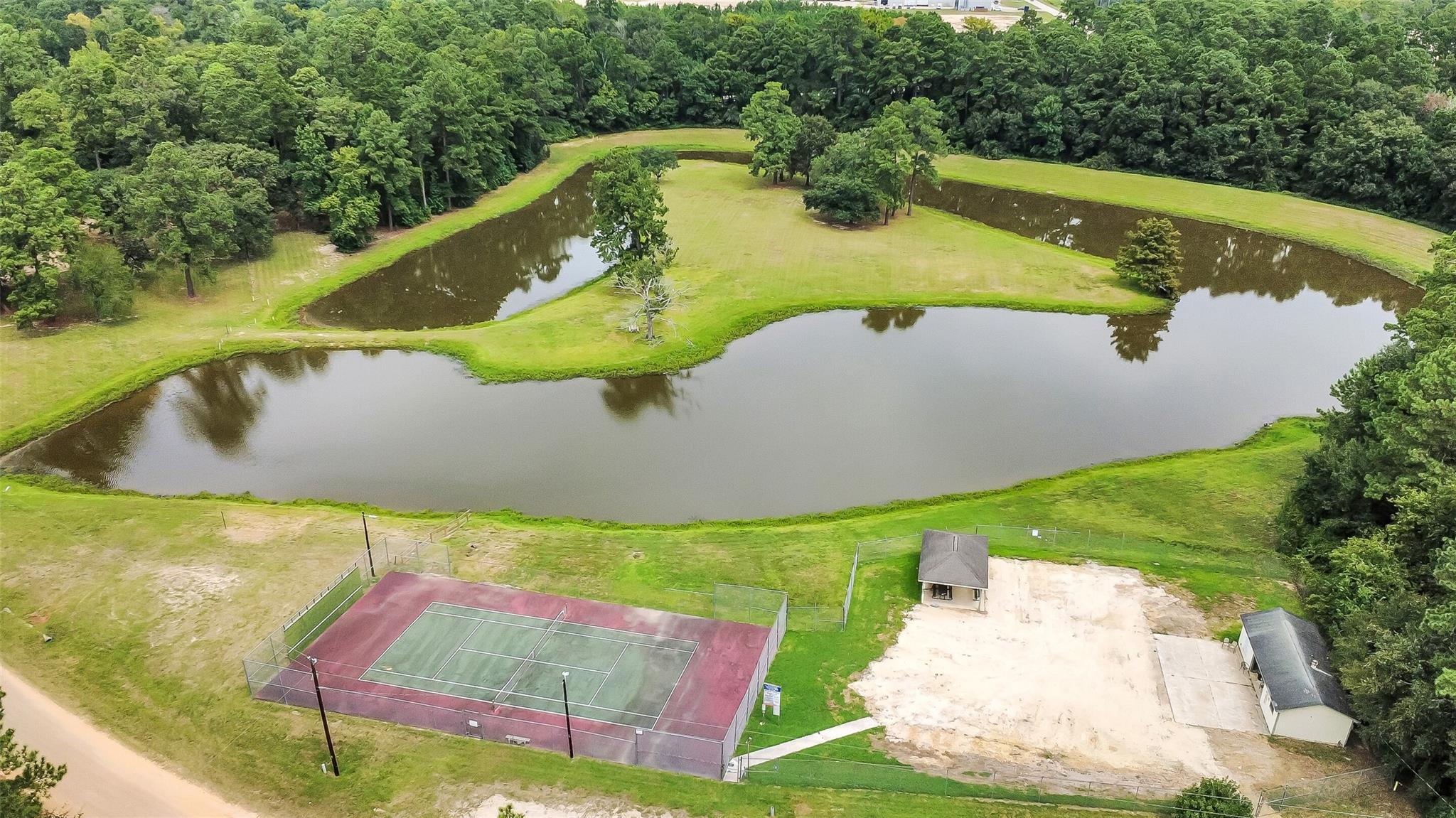 Aerial grounds with several ponds and a fenced tennis court surrounded by trees.