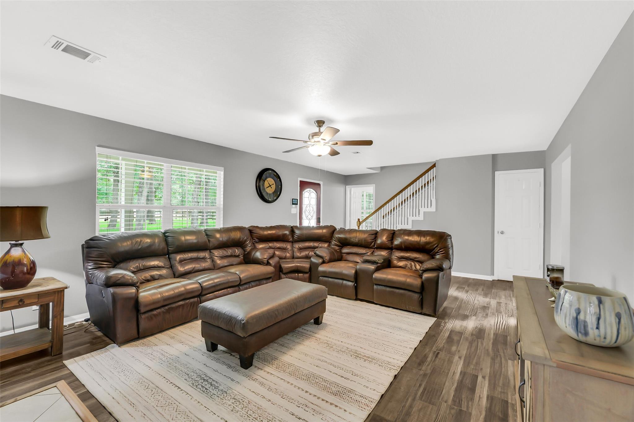 Living room with a brown leather sectional, ottoman, wide window, and staircase.