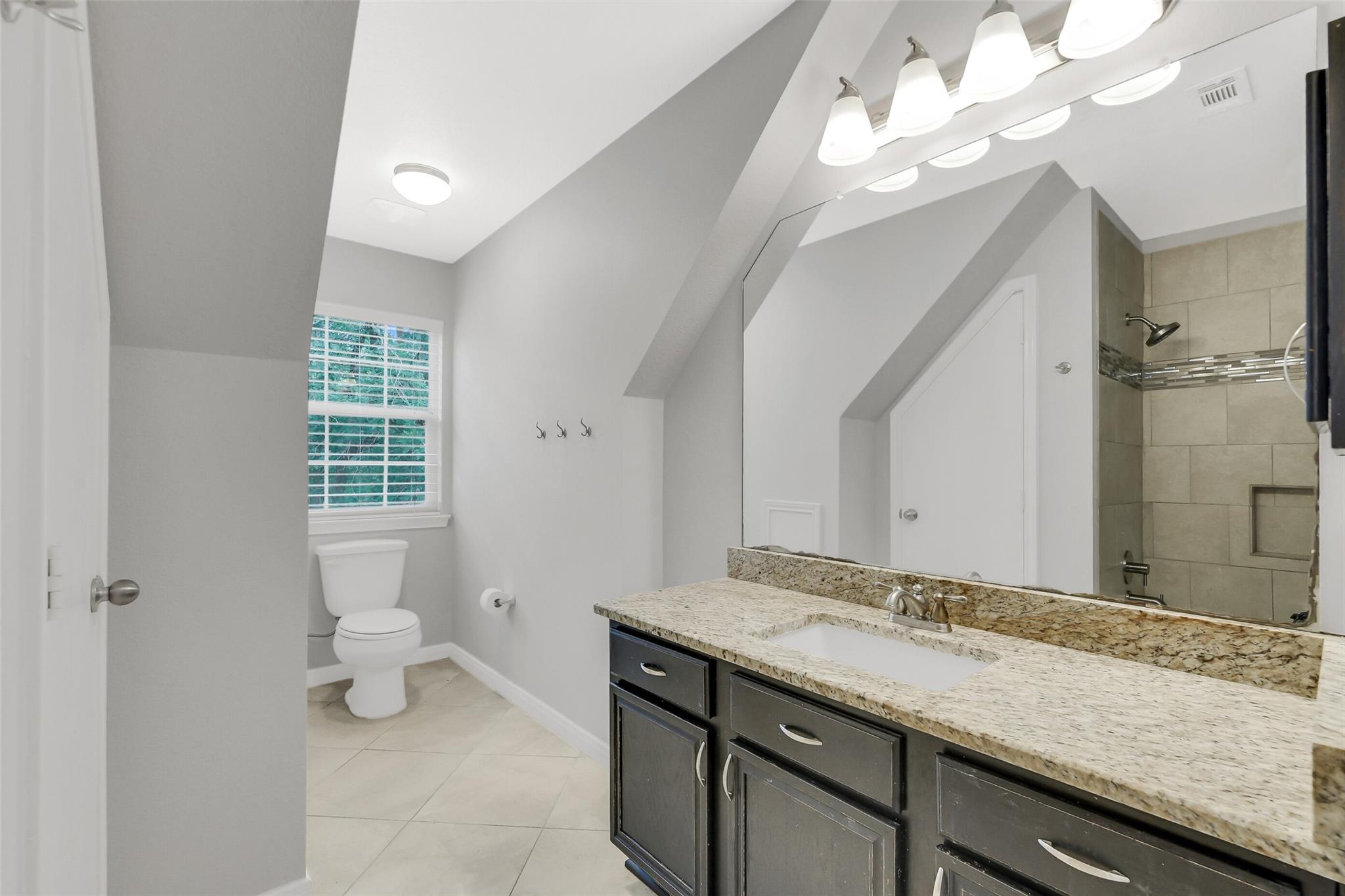Bathroom with dark double vanity, granite countertop, large mirror, and tiled walk-in shower.