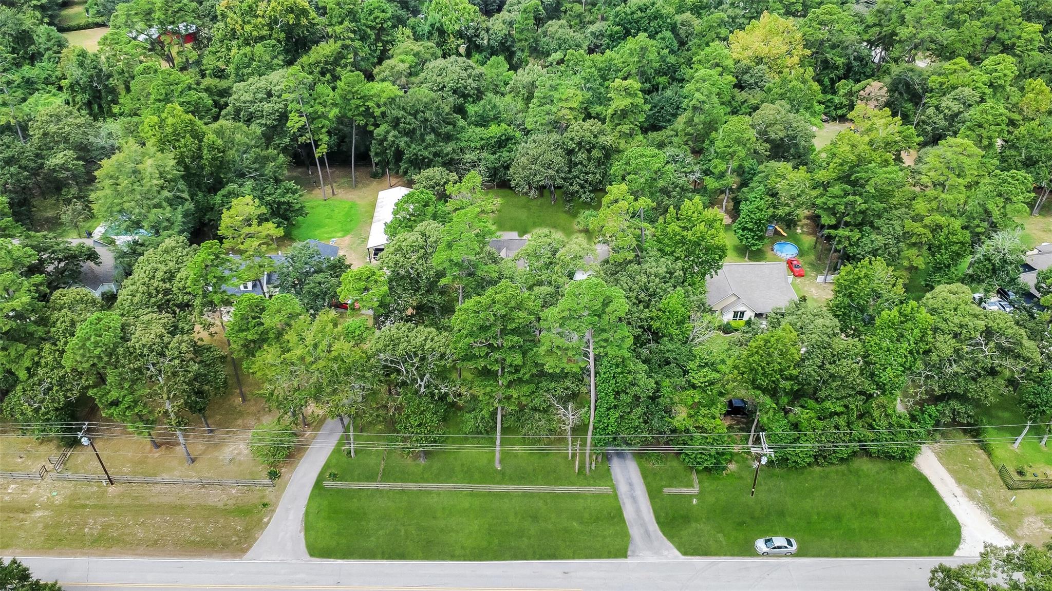 Aerial view of a wooded property with homes, an outbuilding, and a small above-ground pool.