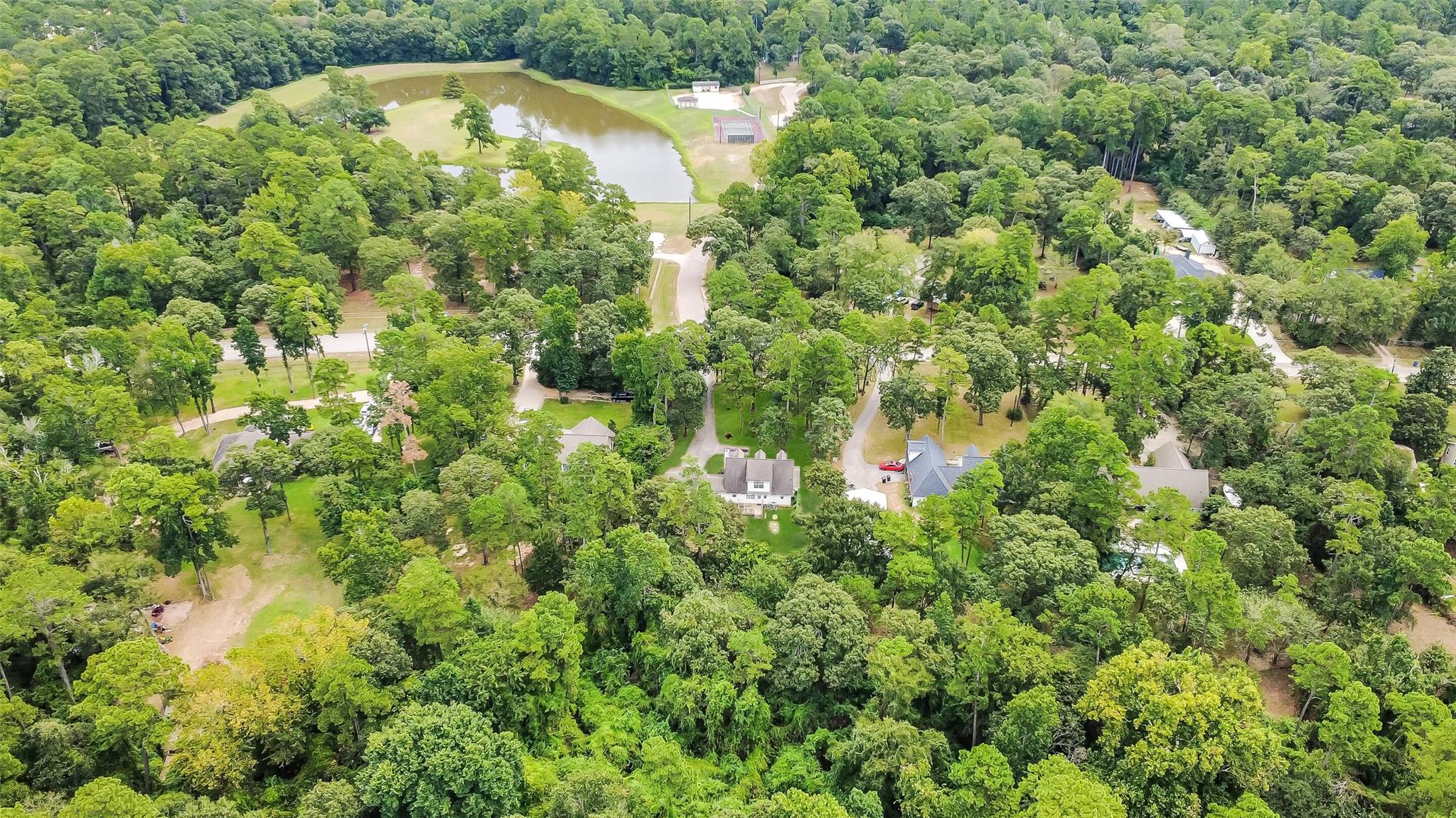 Aerial view of wooded acreage with a large pond and scattered homes.