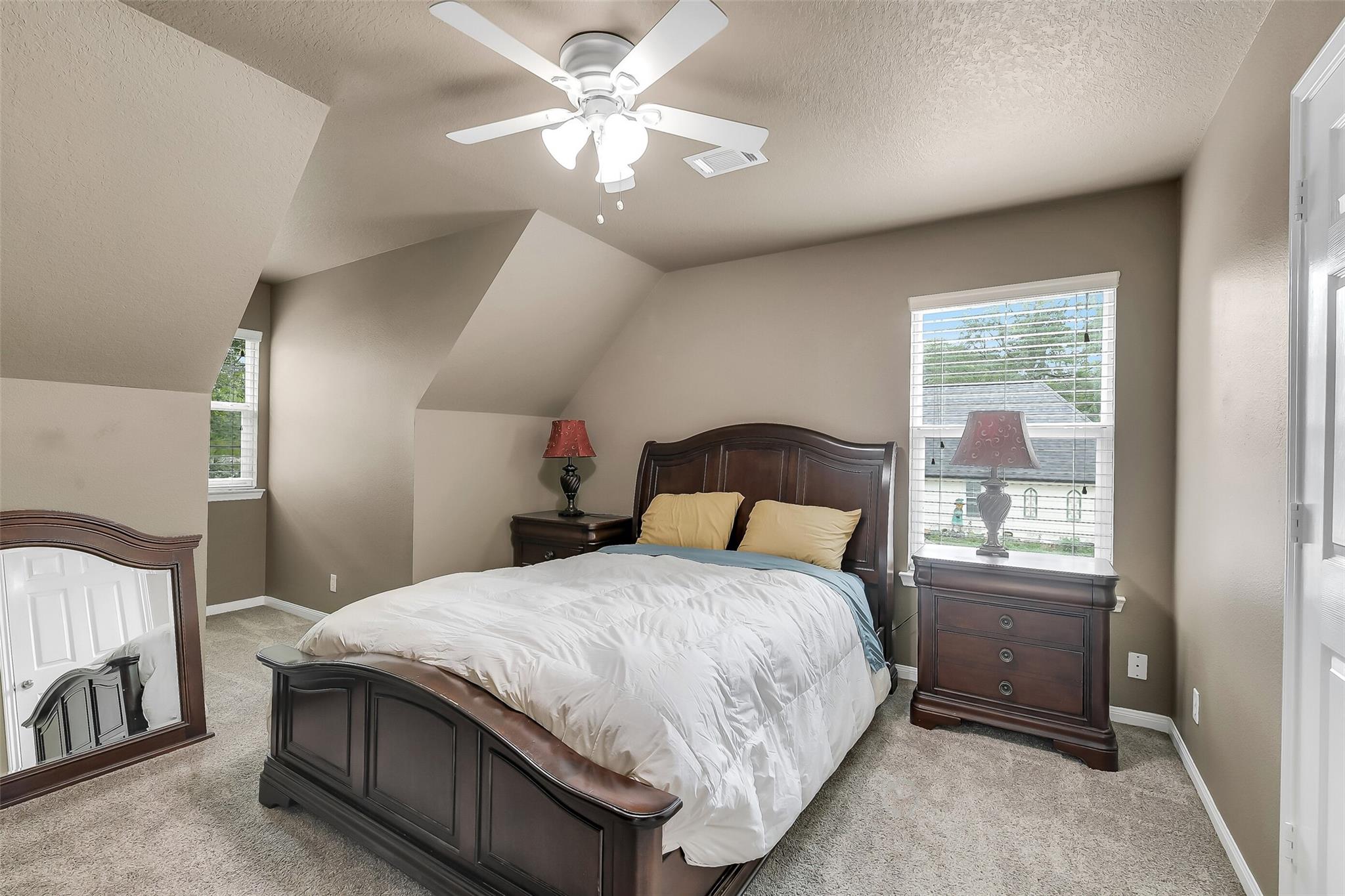 Furnished bedroom with a dark wood bed beneath sloped ceilings and windows with white blinds.