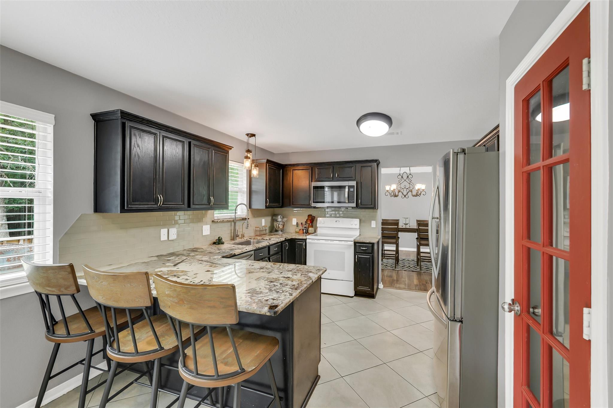 Kitchen with dark cabinets, a marble-patterned island, stainless appliances, and a red glass-paneled door.