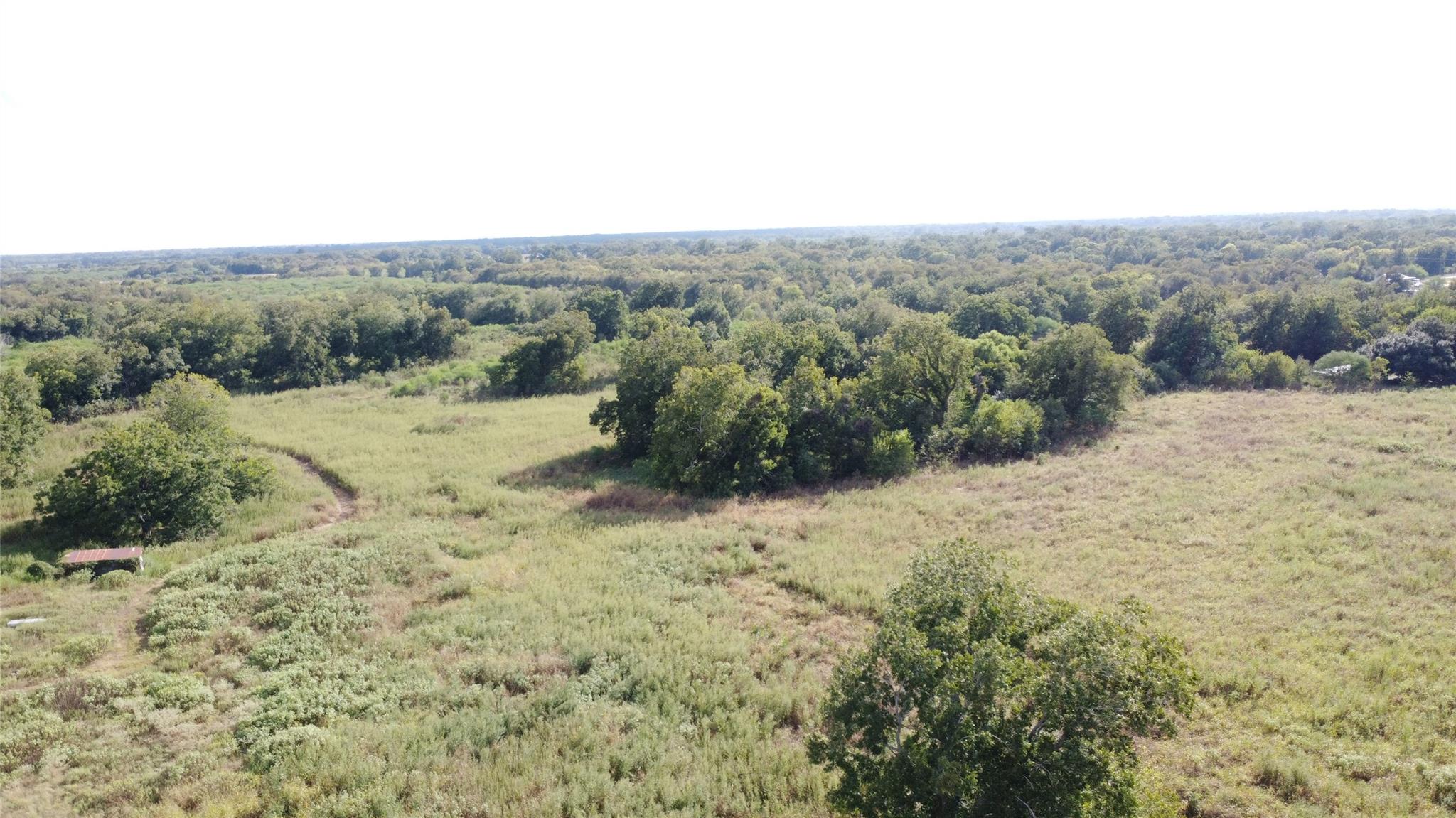 Aerial view of grassy acreage bordered by dense woodland, with a small roofed structure.