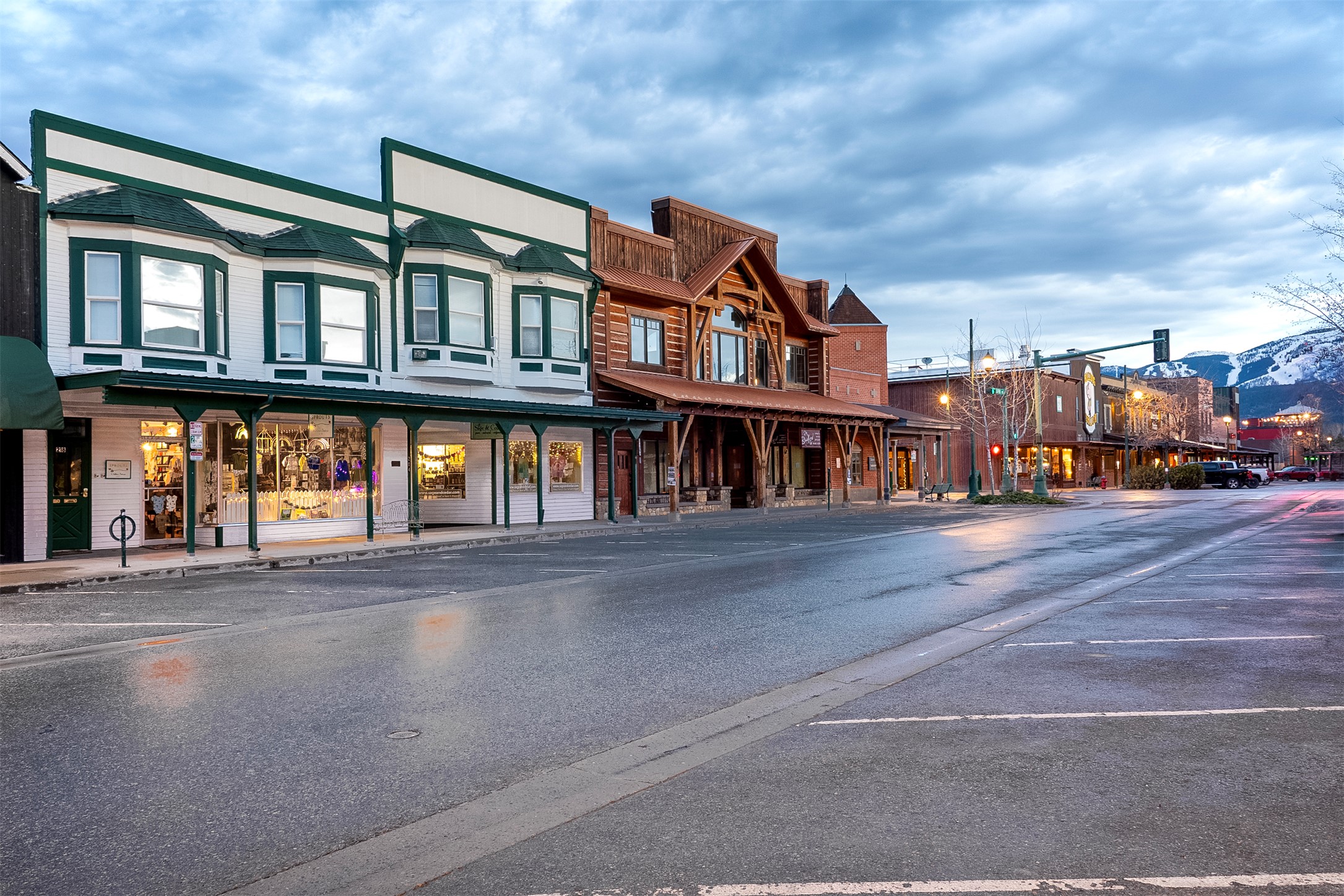 Mountain-town storefronts along a quiet street, with snowy peaks in the distance.