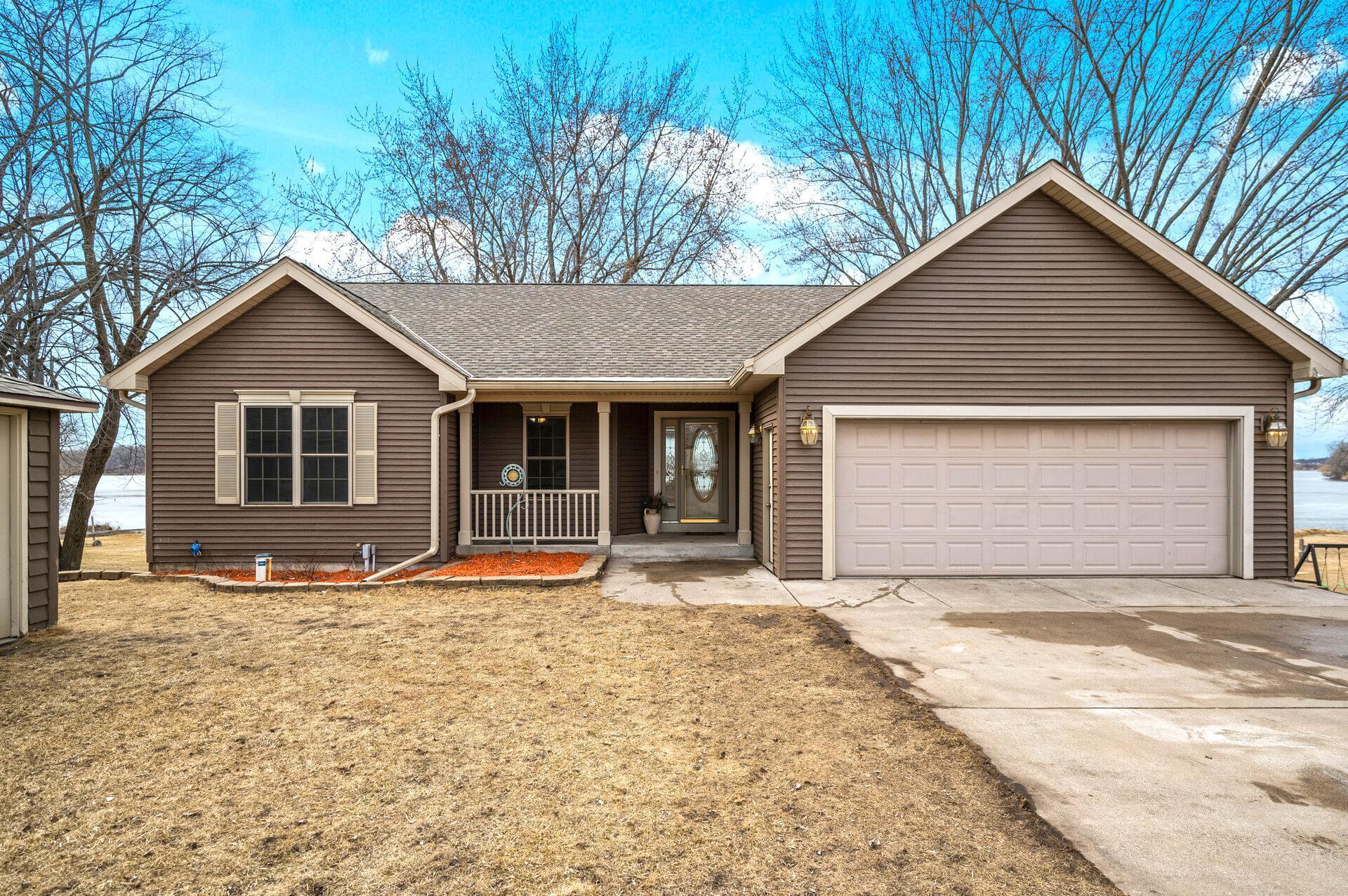 Brown-sided home with a two-car garage and covered entry beside a lake.