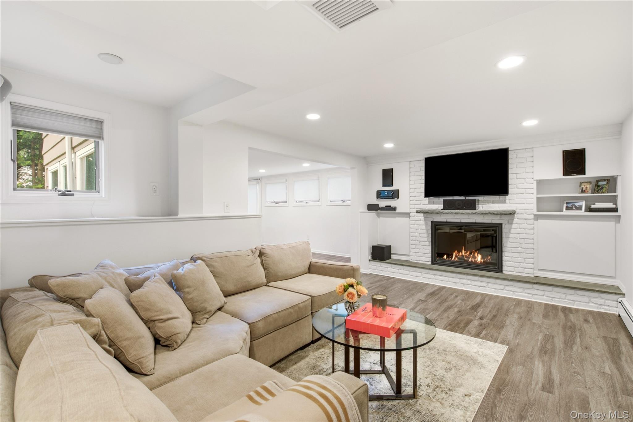 Living room with a beige sectional and a white brick fireplace beneath a mounted television.