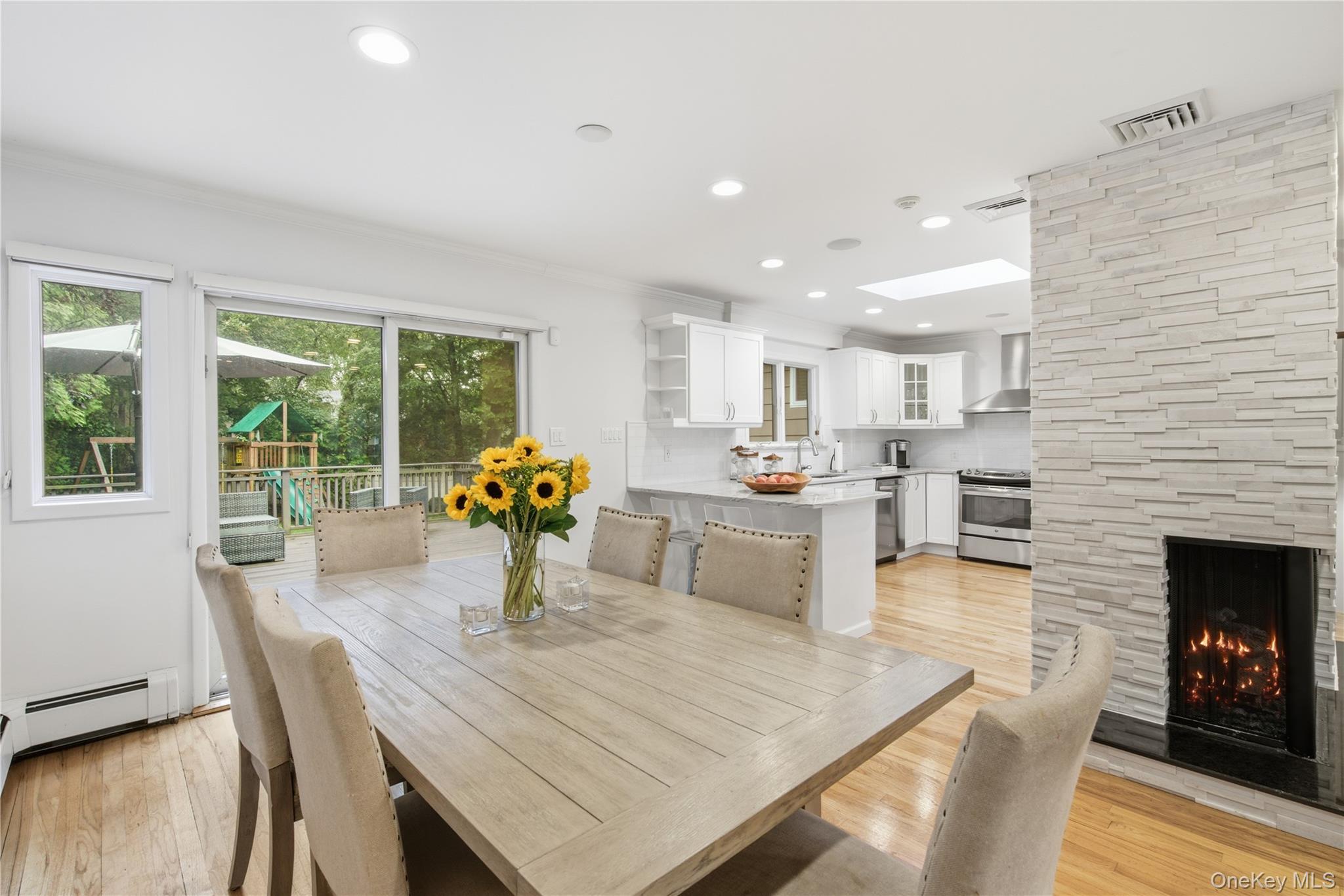 Open-plan dining room and kitchen with a large wood table, stone fireplace, and sliding doors to a deck.