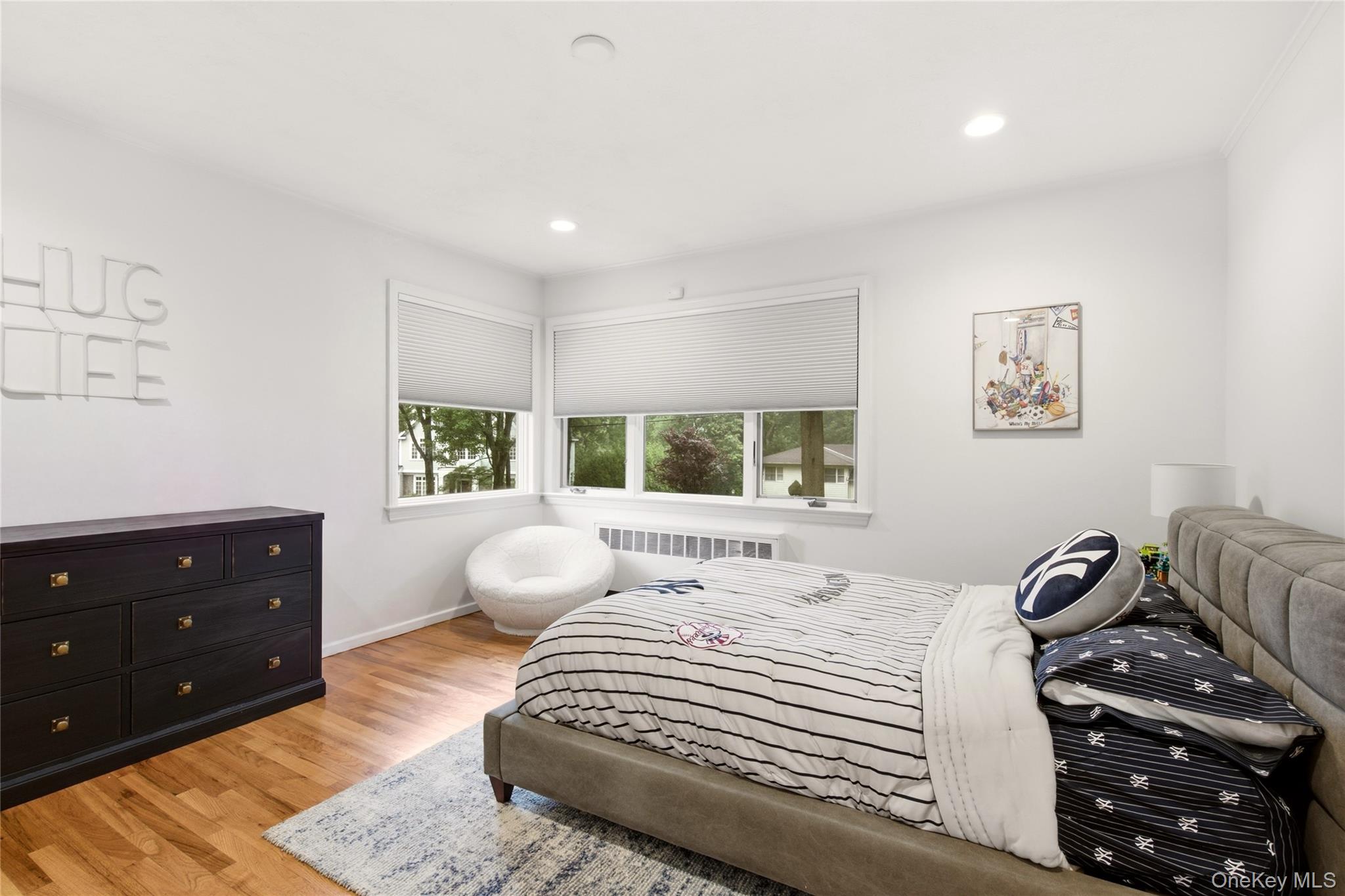 Furnished bedroom with a gray upholstered bed, striped bedding, hardwood floors, and corner windows.