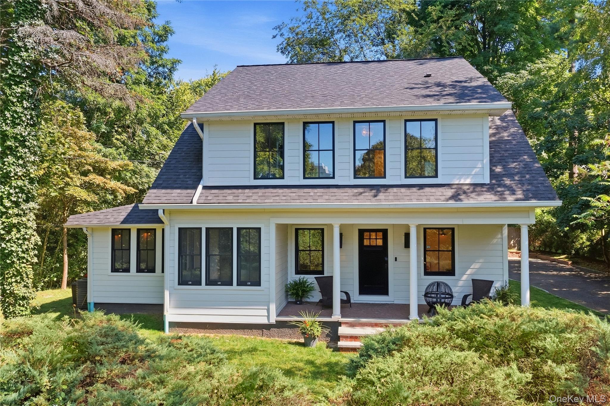 White two-story house with a columned front porch, dark-trimmed windows, and leafy surroundings.