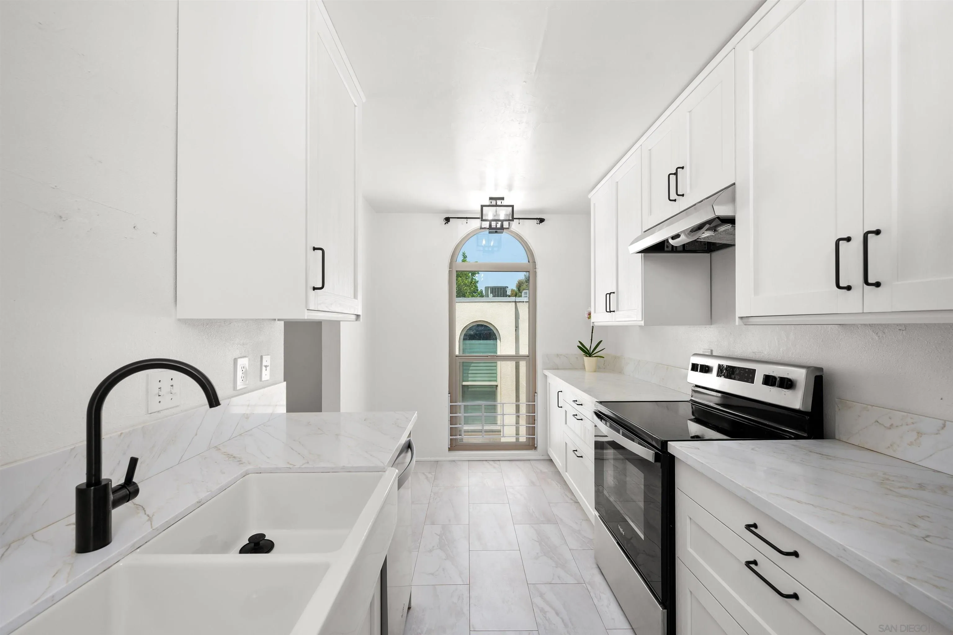 Bright white kitchen with marble-look counters, black fixtures, and an arched window.